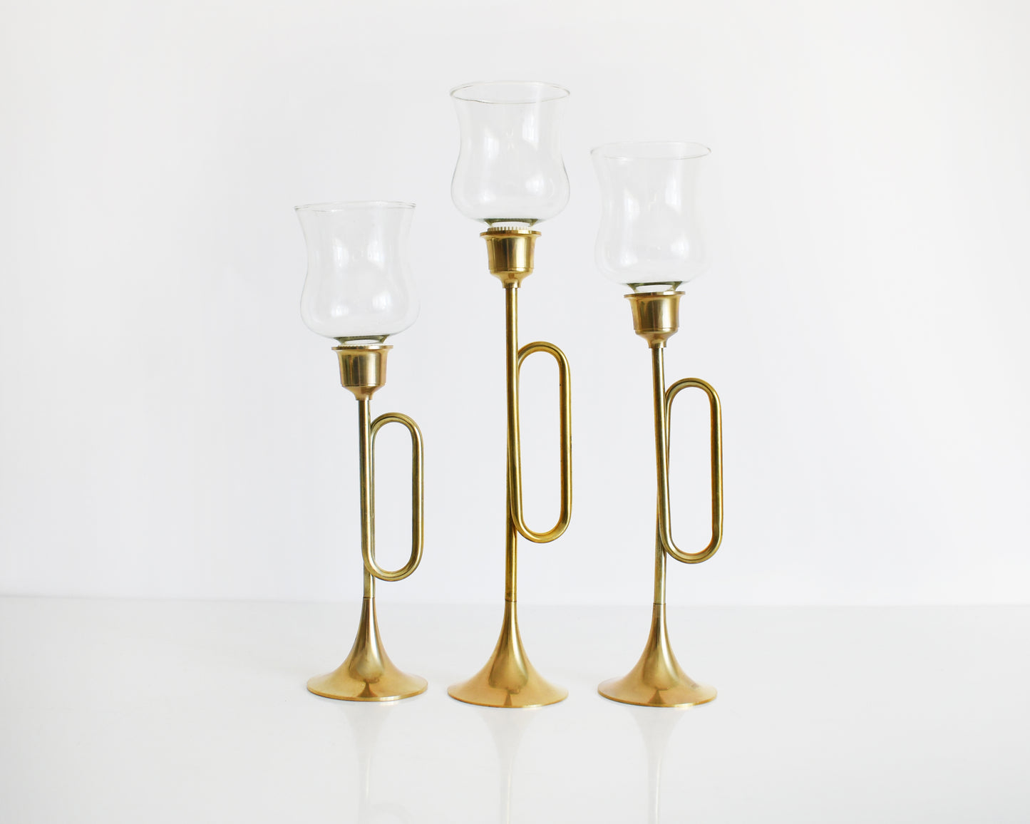 Three vintage brass bugle/horn candlesticks that has clear class votives on top.