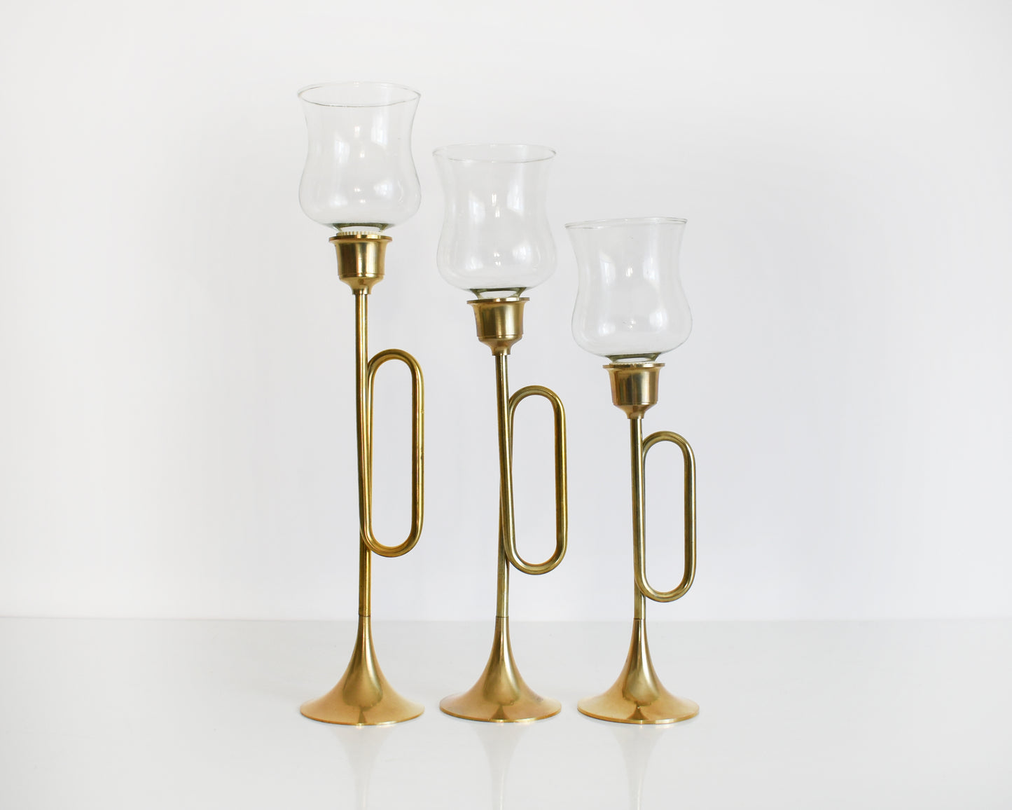 Three vintage brass bugle/horn candlesticks that has clear class votives on top.