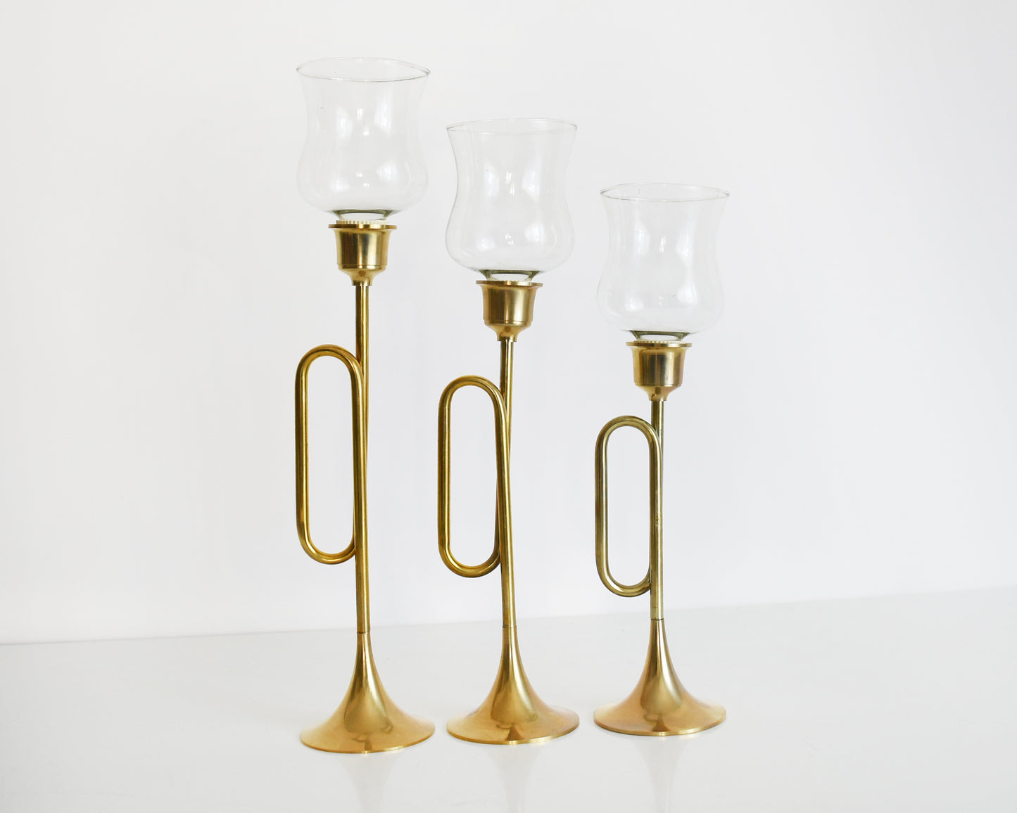 Three vintage brass bugle/horn candlesticks that has clear class votives on top.