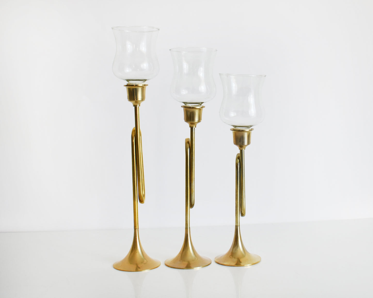 Side view of three vintage brass bugle/horn candlesticks that has clear class votives on top.