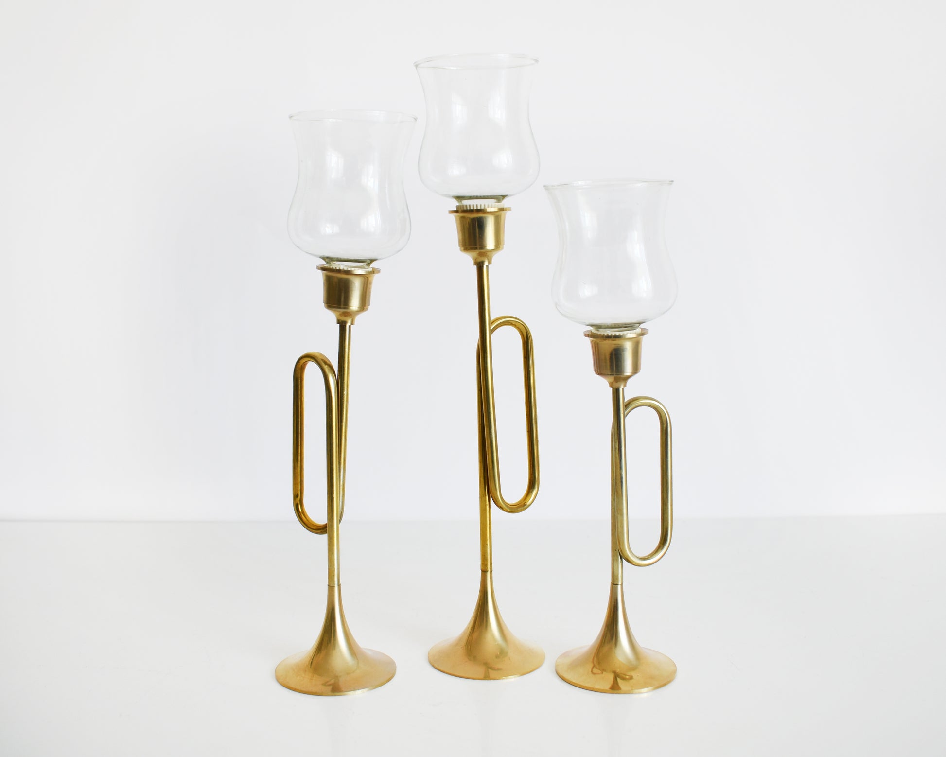 Three vintage brass bugle/horn candlesticks that has clear class votives on top.