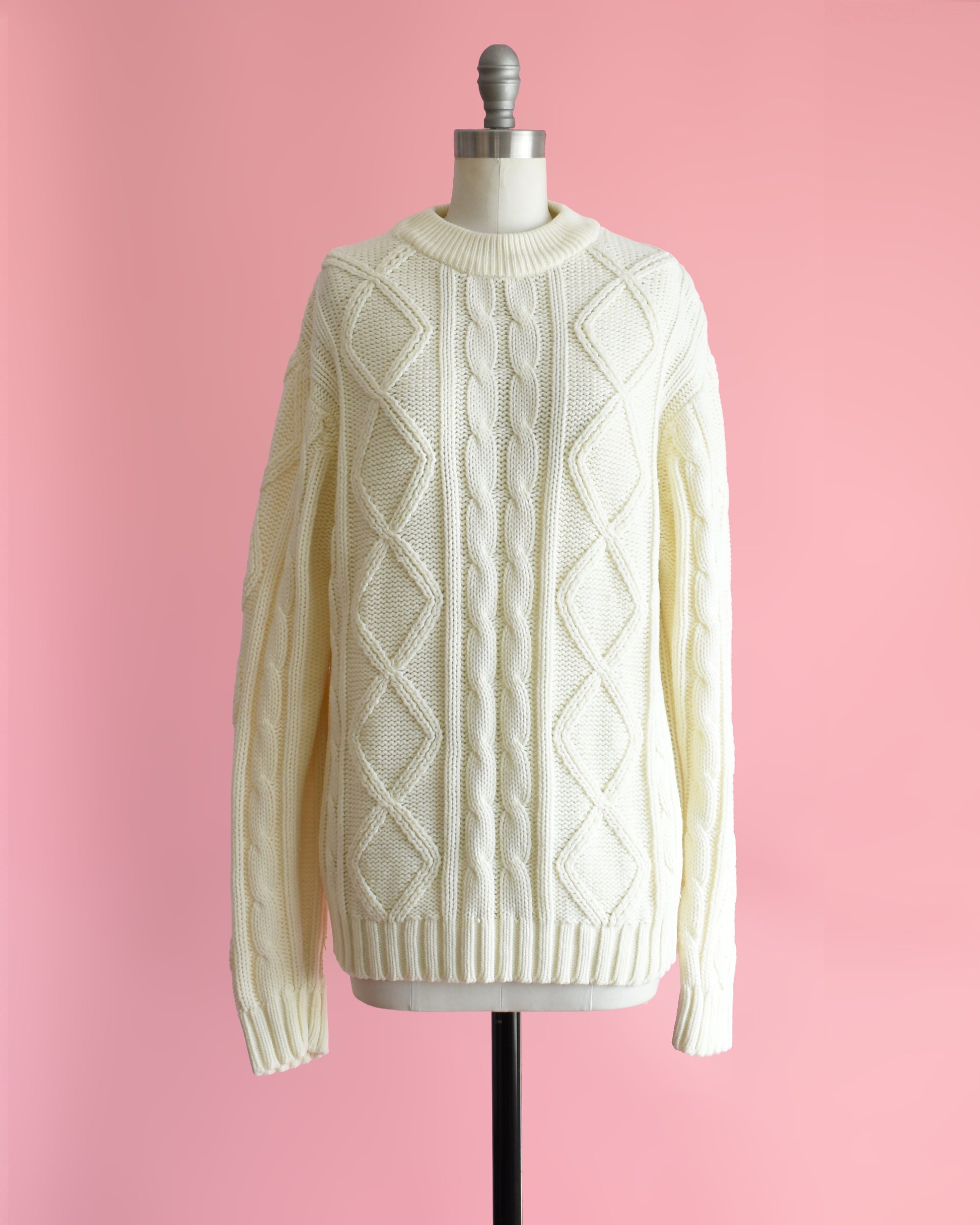 a vintage 1970s cream cable knit sweater on a dress form against a pink background