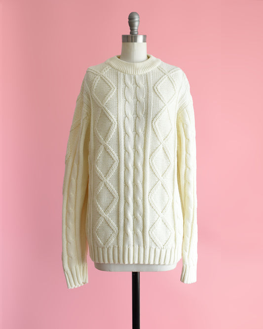 a vintage 1970s cream cable knit sweater on a dress form against a pink background