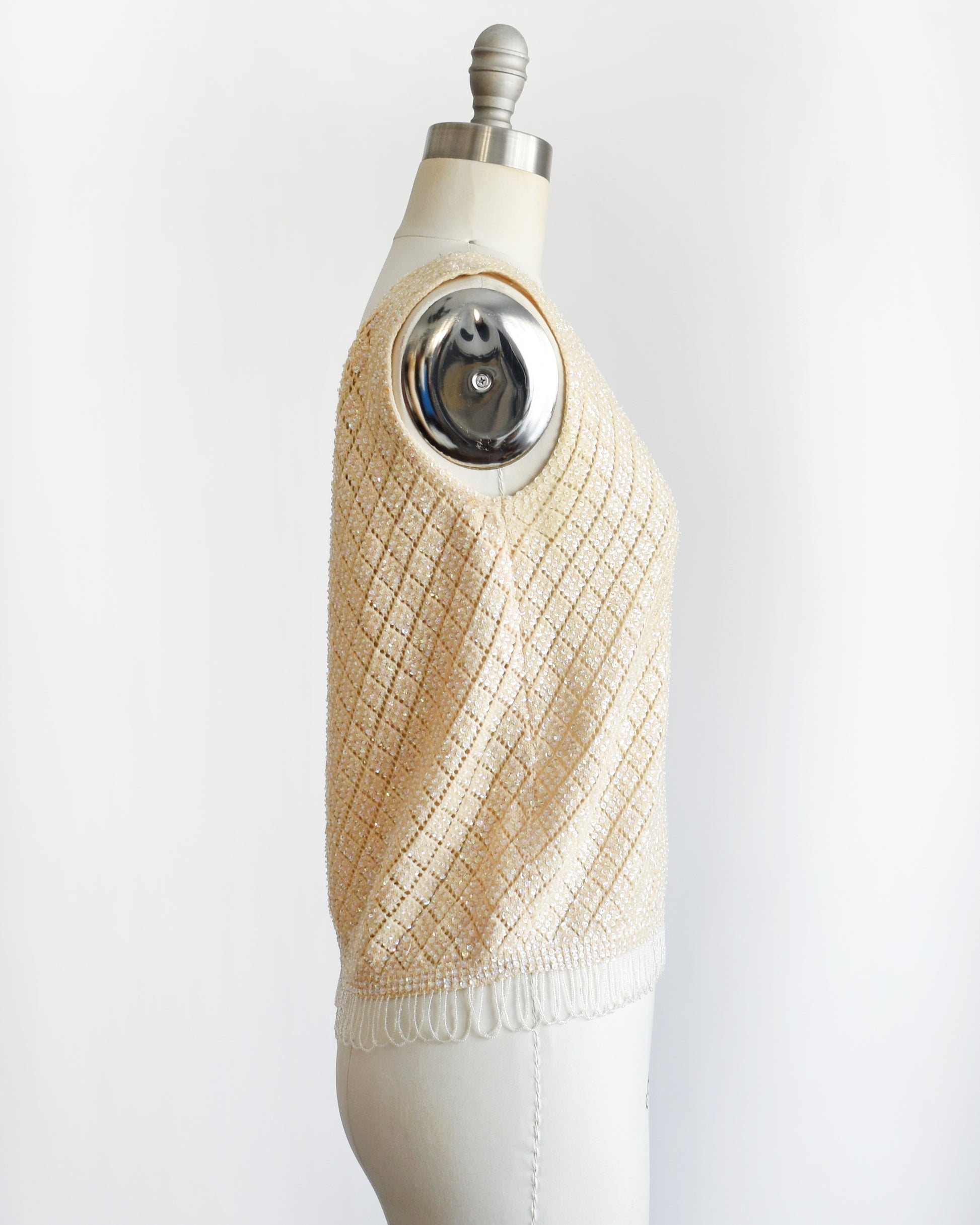 side view of a vintage 1960s cream sequin and beaded top on a mannequin against a white background