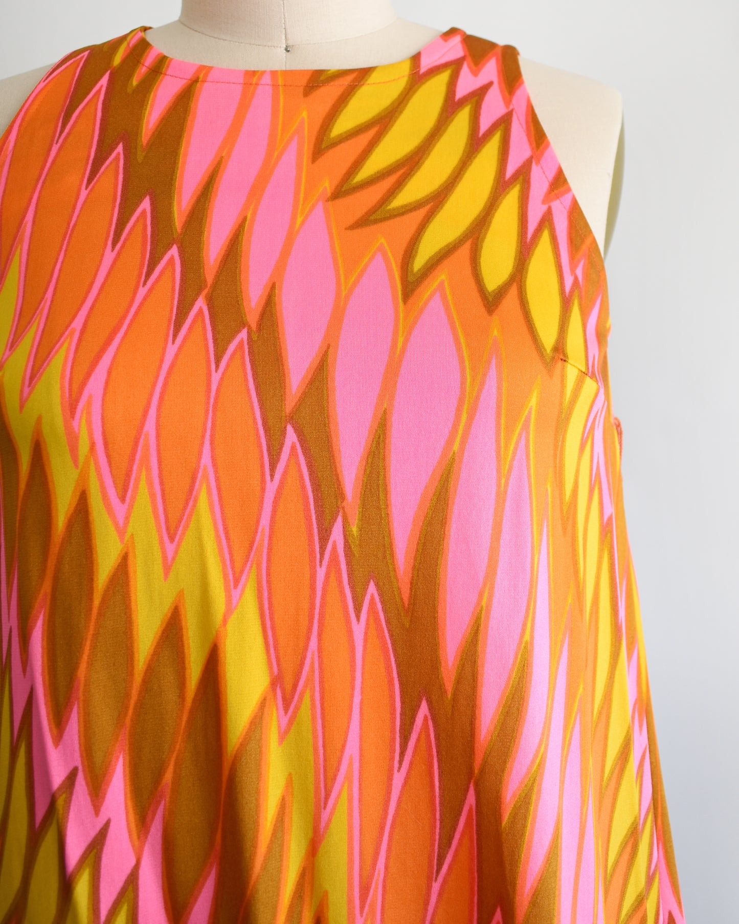close up of the bodice of  a vintage 1960s mini dress that has a psychedelic print in orange, pink, yellow, and brown