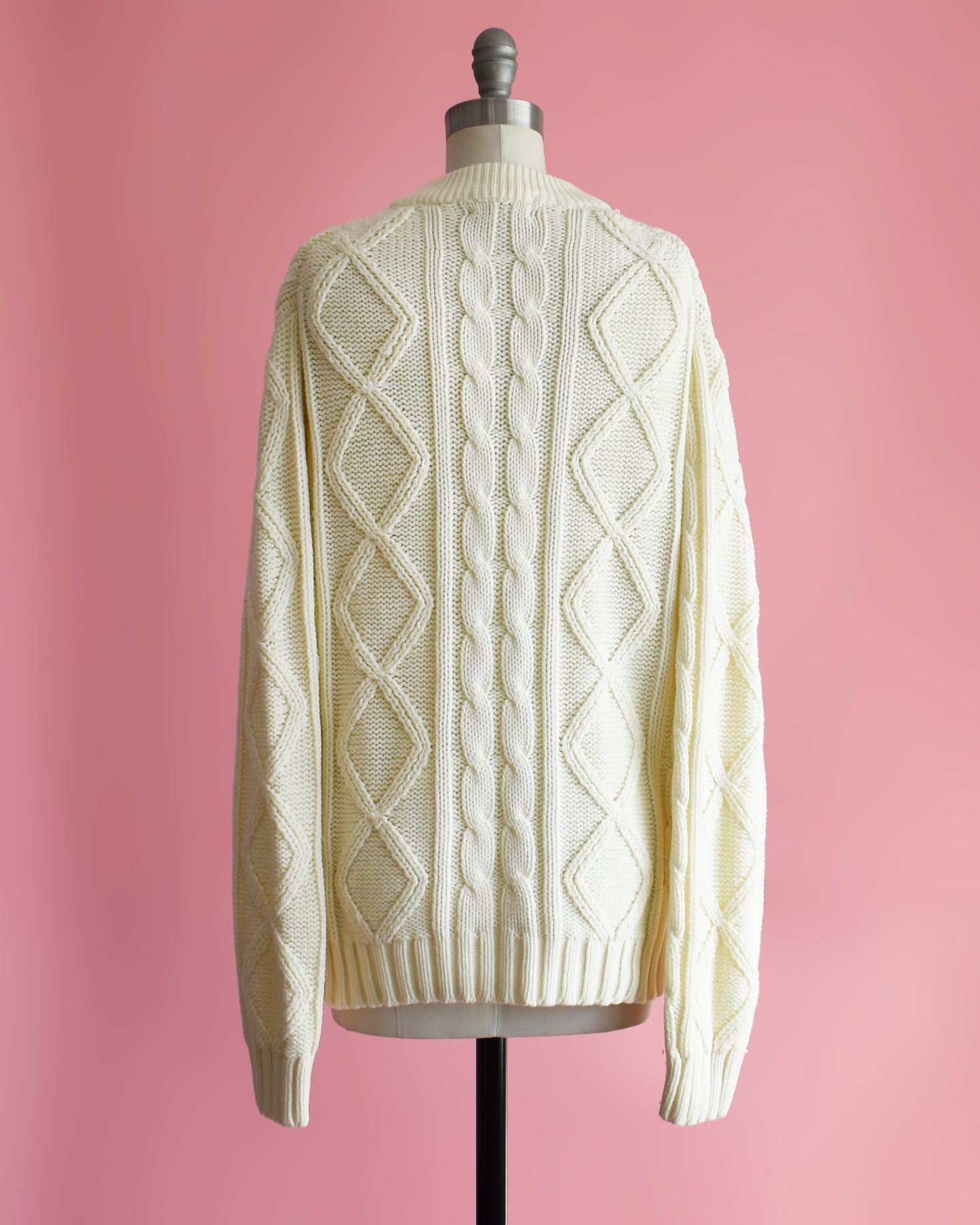 back view of a vintage 1970s cream cable knit sweater on a dress form against a pink background