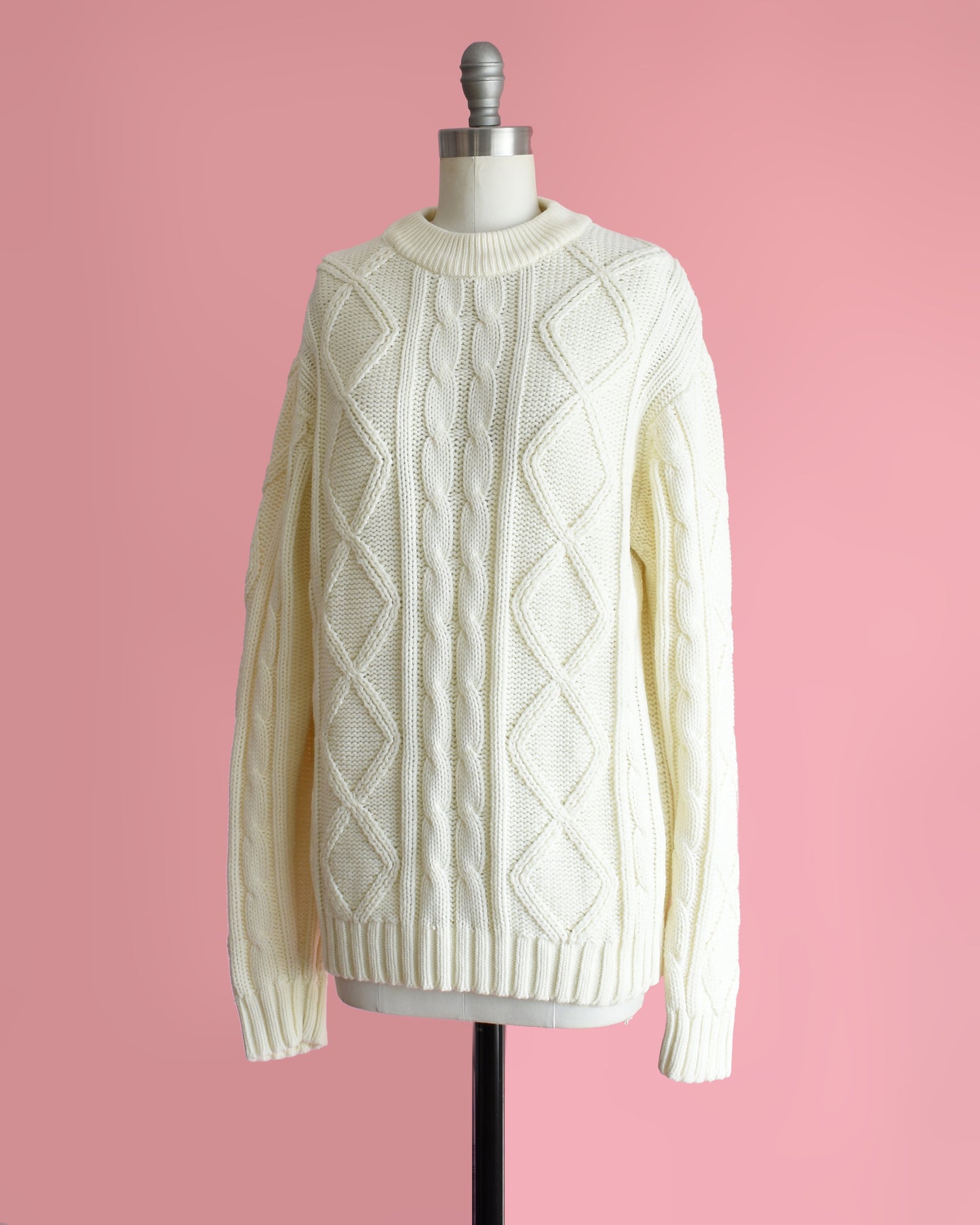 side front view of a vintage 1970s cream cable knit sweater on a dress form against a pink background