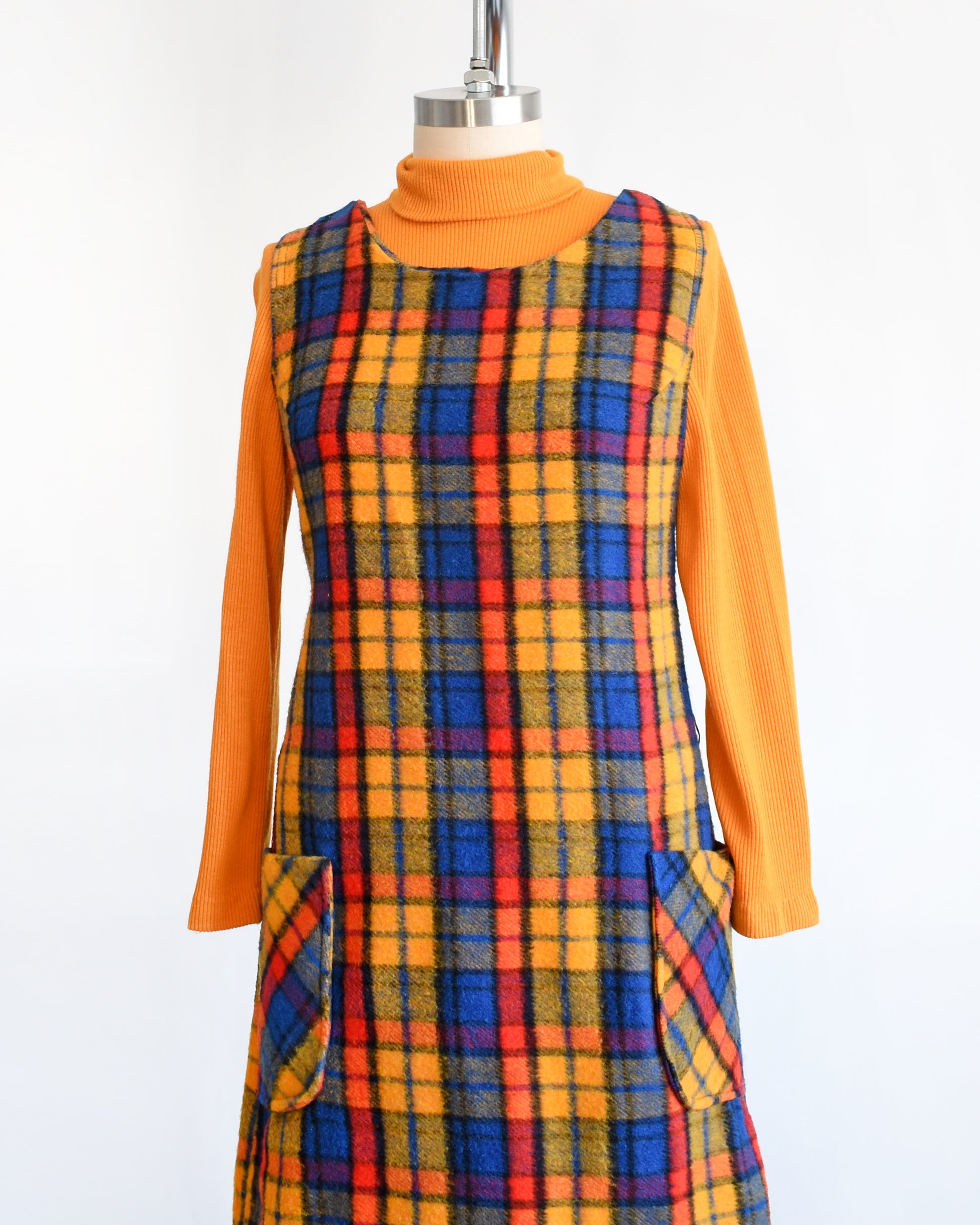 side front view of a vintage 1970s orange, blue, and red plaid pinafore dress with an orange turtleneck underneath