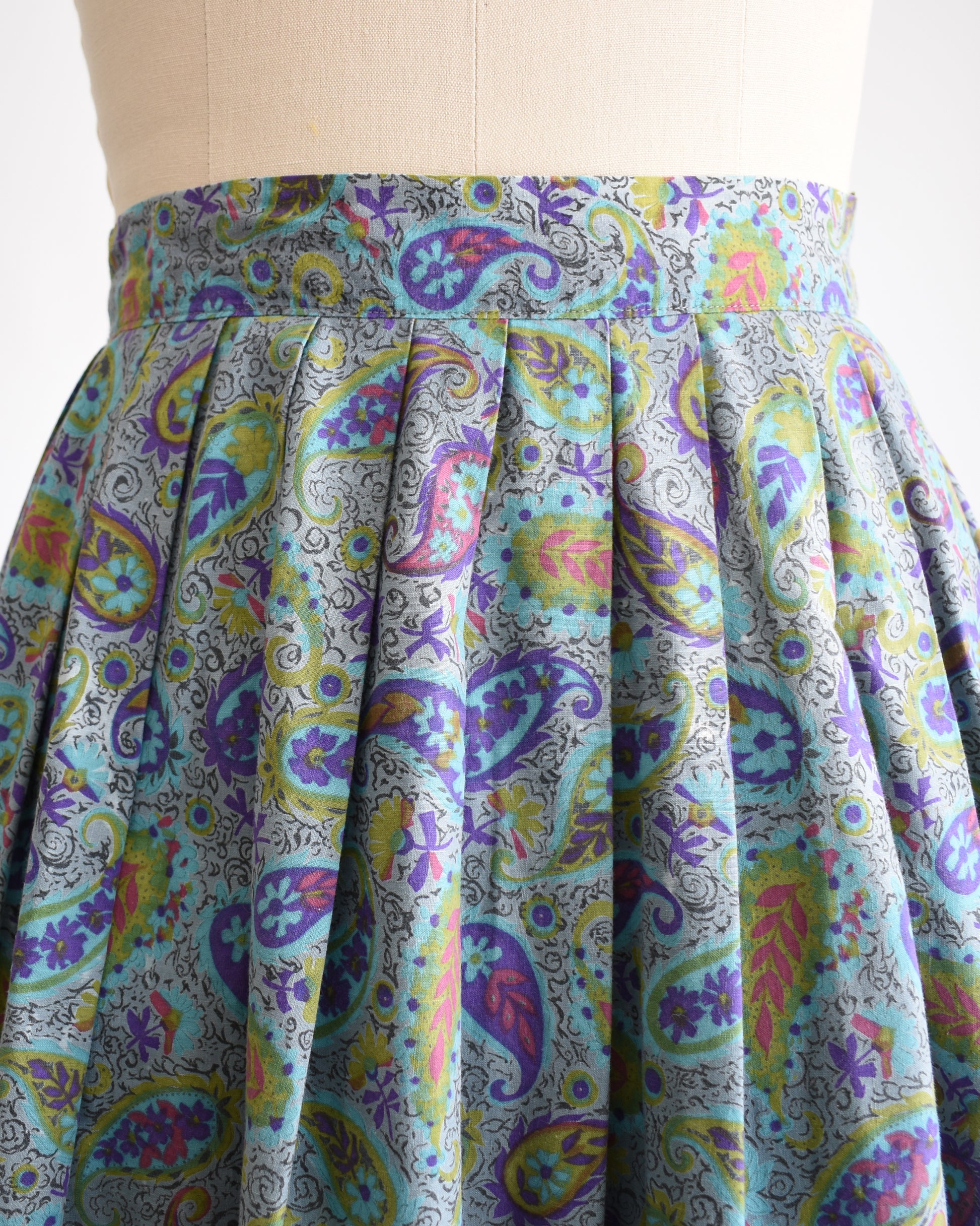 close up of the pleated waist on a vintage 1950s floral paisley skirt on a mannequin against a white background