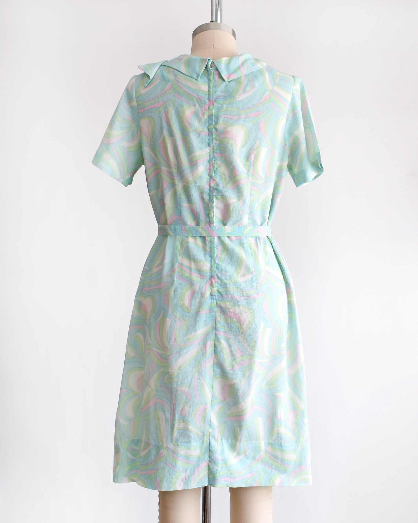 back view of a vintage light blue dress with a swirl pattern on a mannequin against a white background