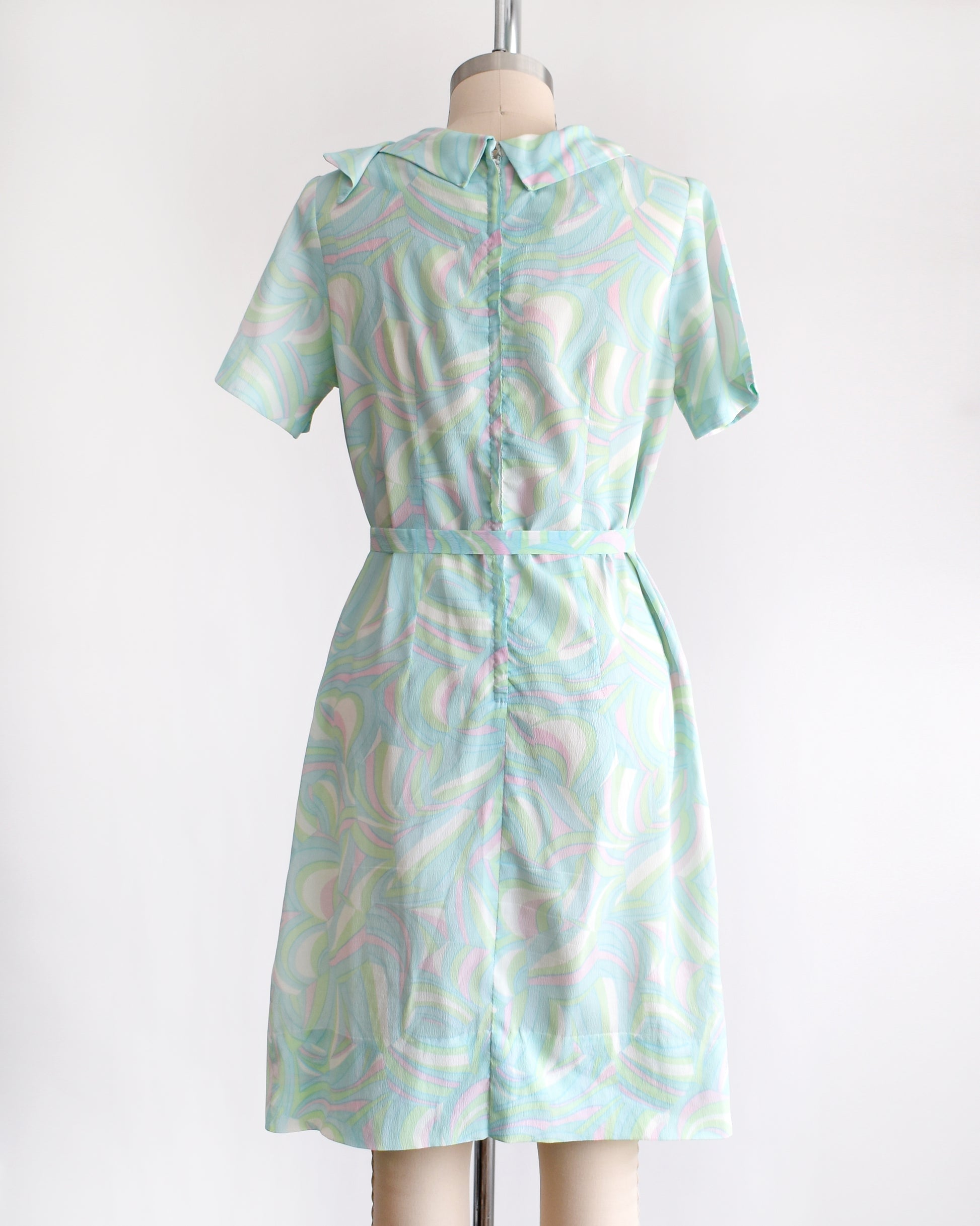 back view of a vintage light blue dress with a swirl pattern on a mannequin against a white background