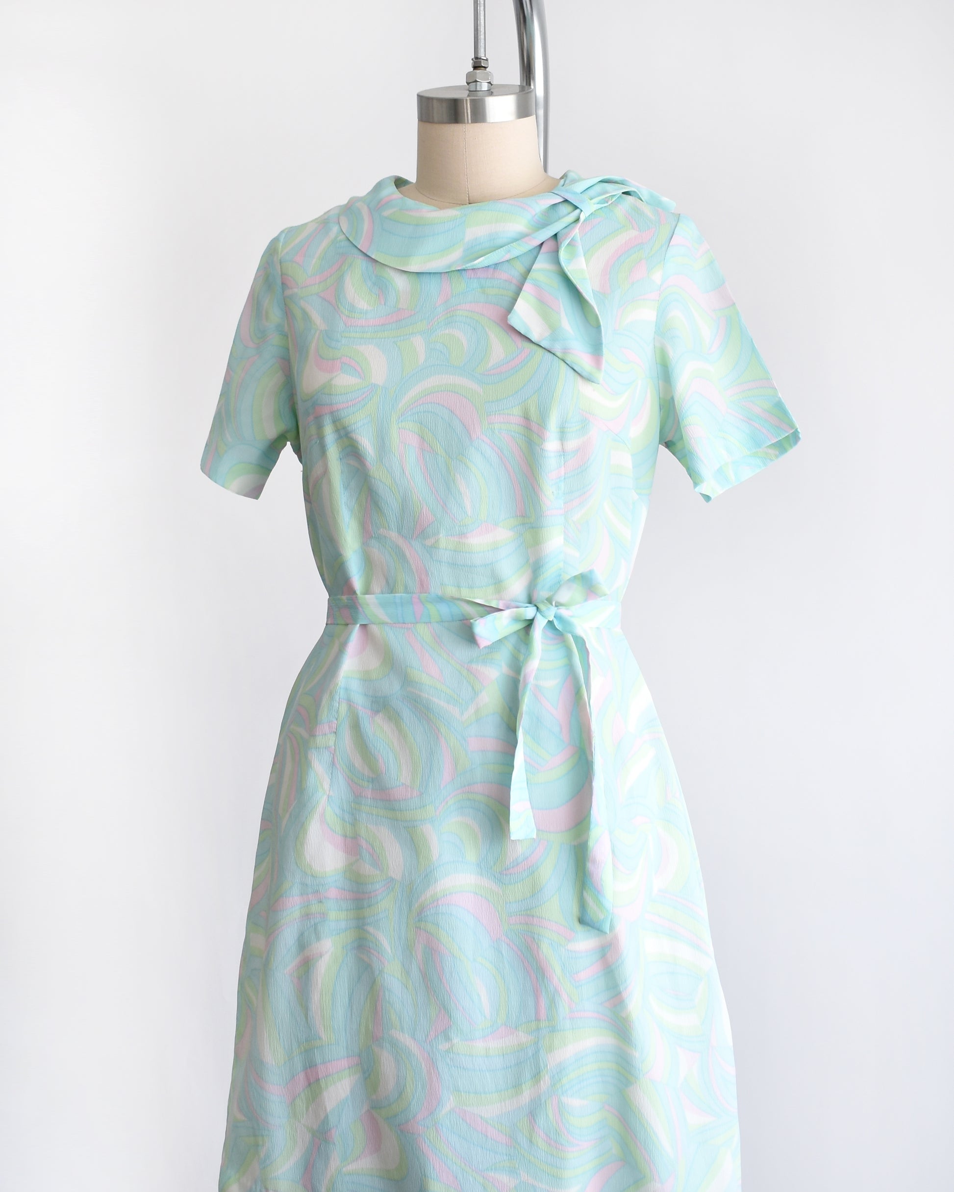 side front view of a vintage light blue dress with a swirl pattern on a mannequin against a white background