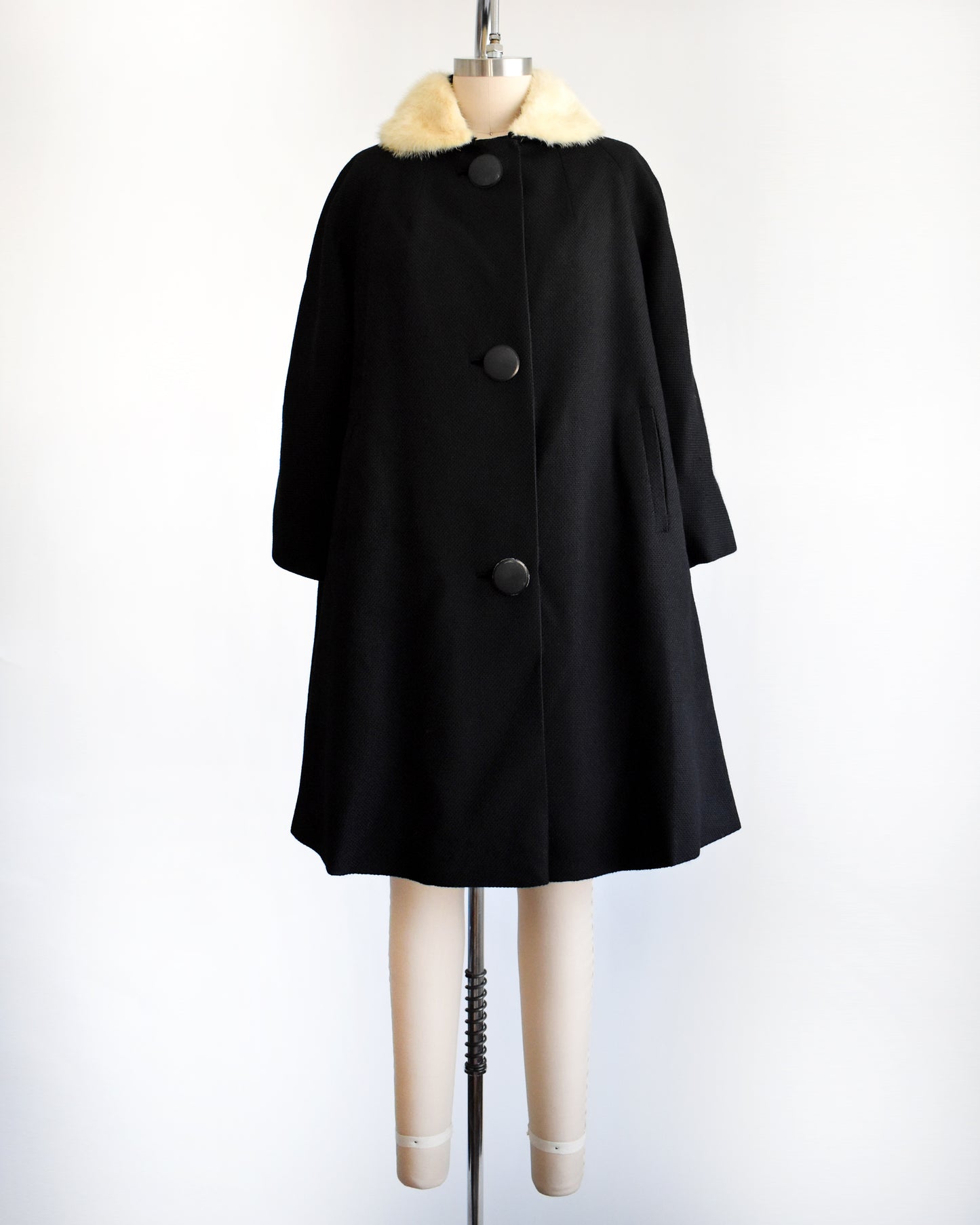 a vintage 1950s black wool coat with fur collar on a mannequin against a white background
