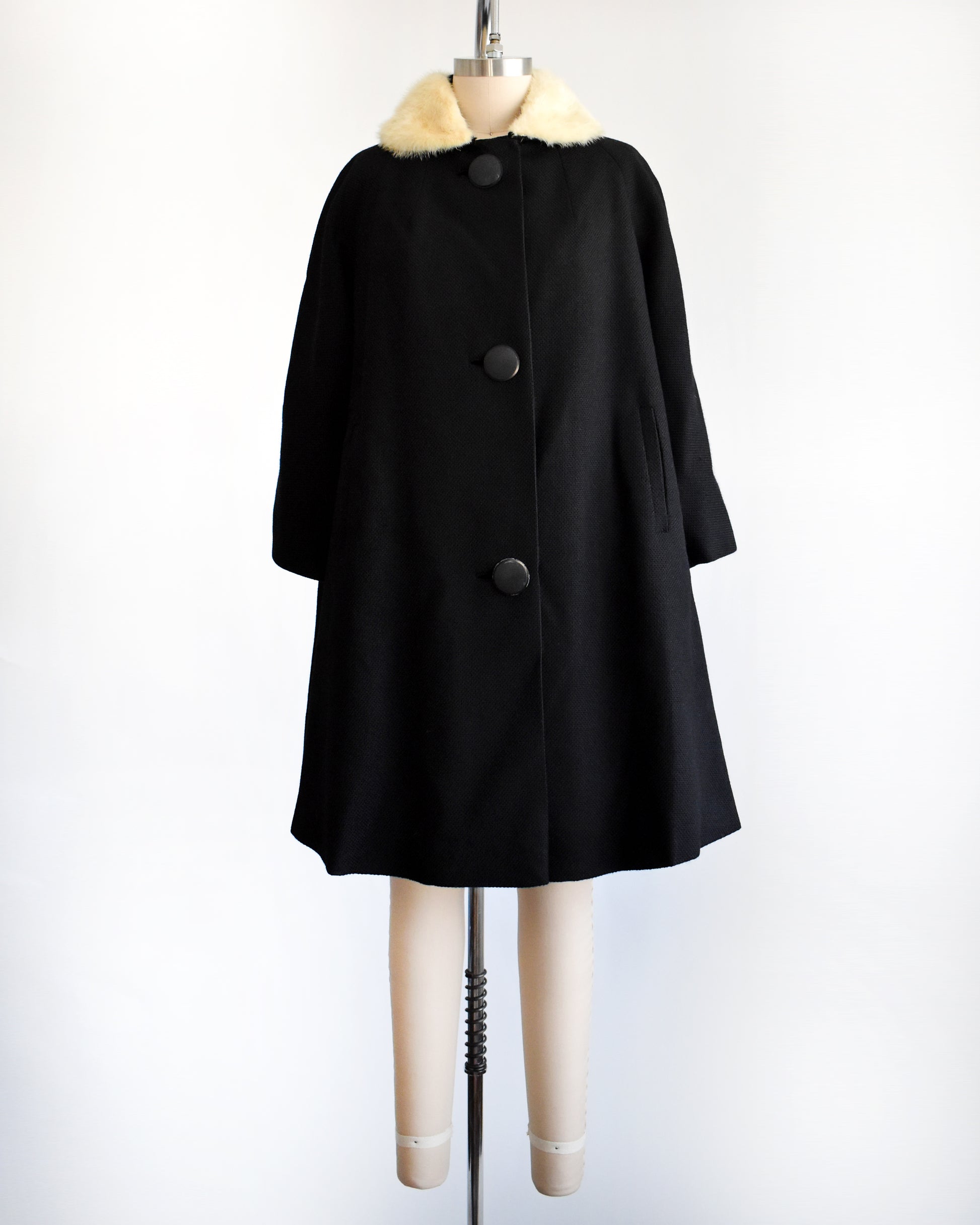 a vintage 1950s black wool coat with fur collar on a mannequin against a white background