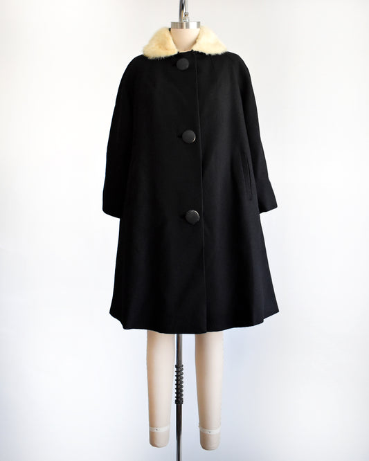 a vintage 1950s black wool coat with fur collar on a mannequin against a white background