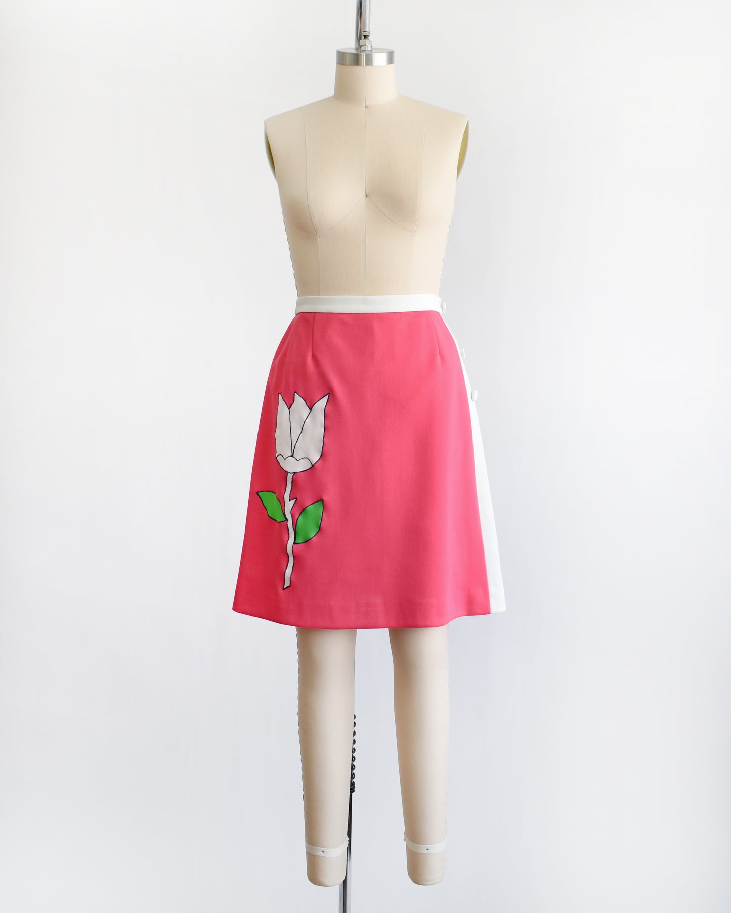a vintage 1970s pink skirt/skort with a white tulip design on a mannequin against a white background
