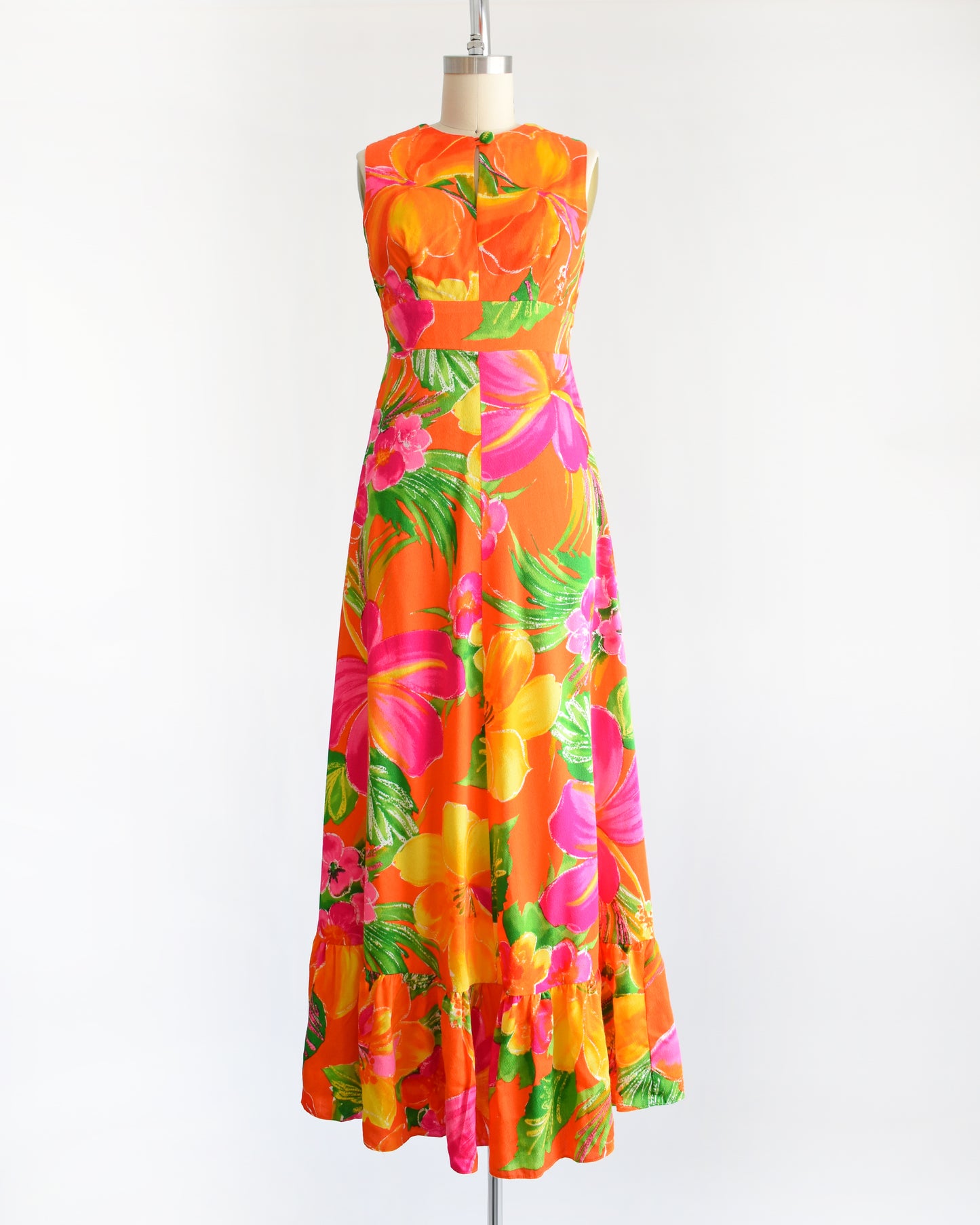 A vintage 1970s Hawaiian maxi dress that has bold floral print in various shades of oranges, pinks, greens, and white.