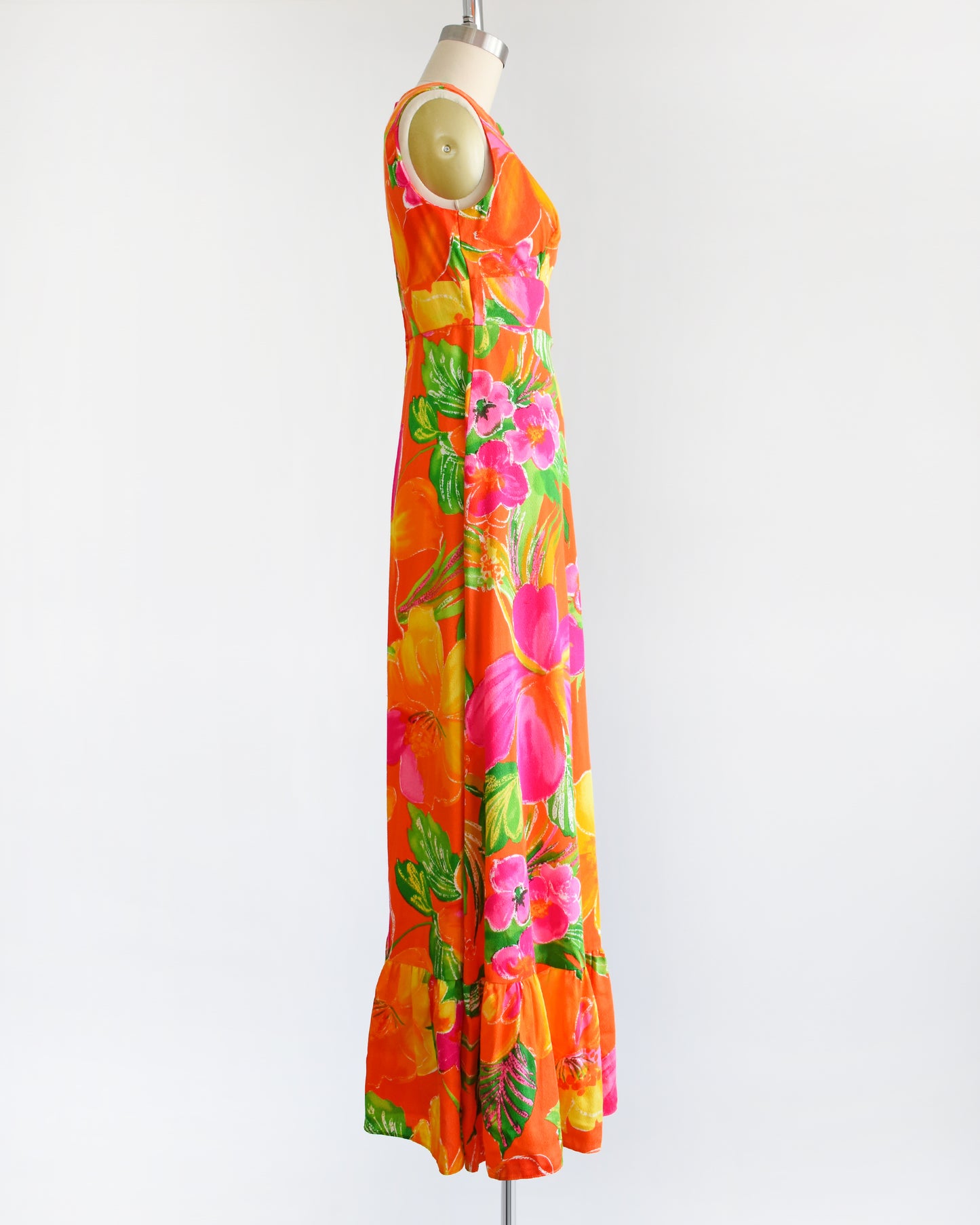 side view of avintage 1970s Hawaiian maxi dress that has bold floral print in various shades of oranges, pinks, greens, and white.