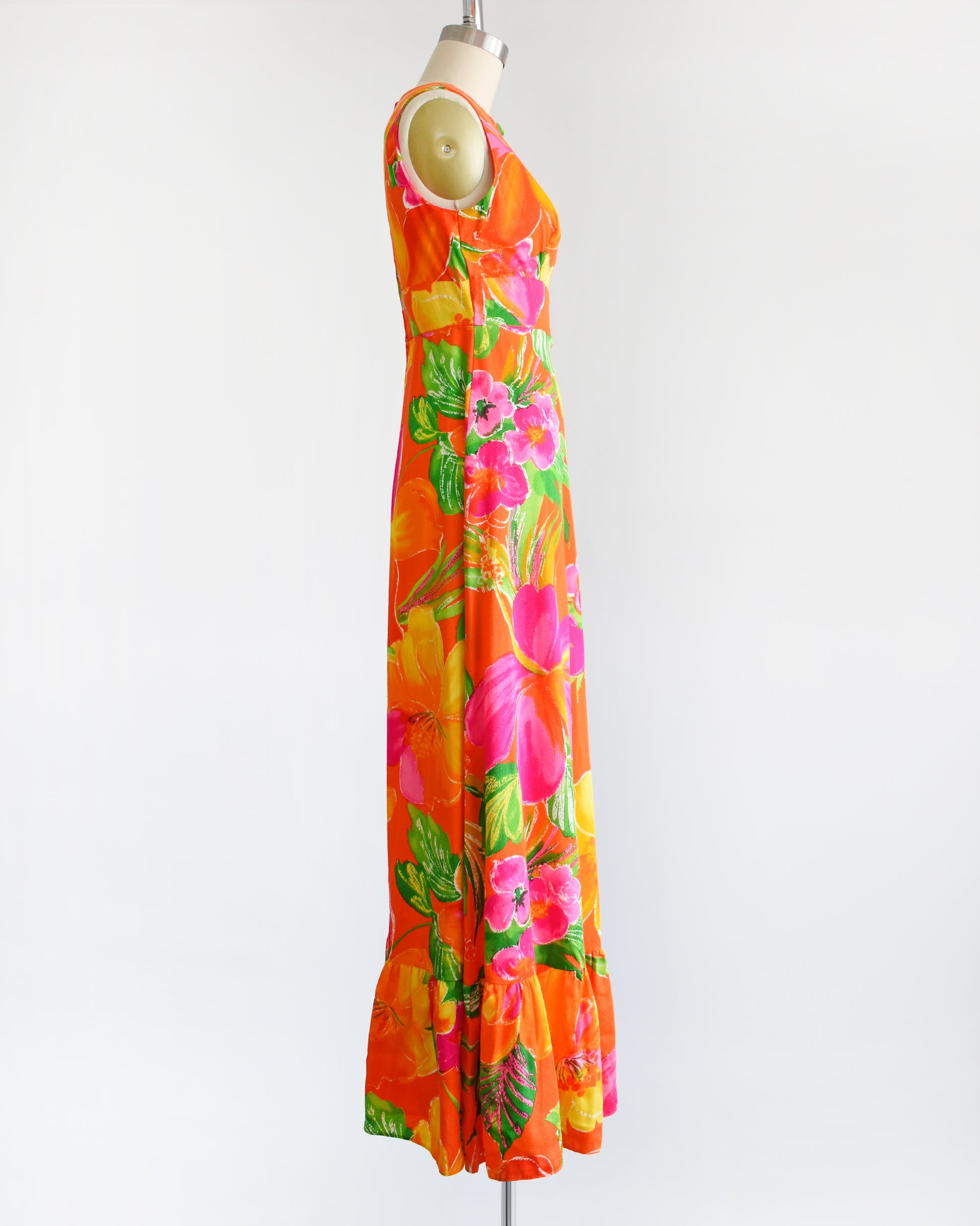 side view of avintage 1970s Hawaiian maxi dress that has bold floral print in various shades of oranges, pinks, greens, and white.