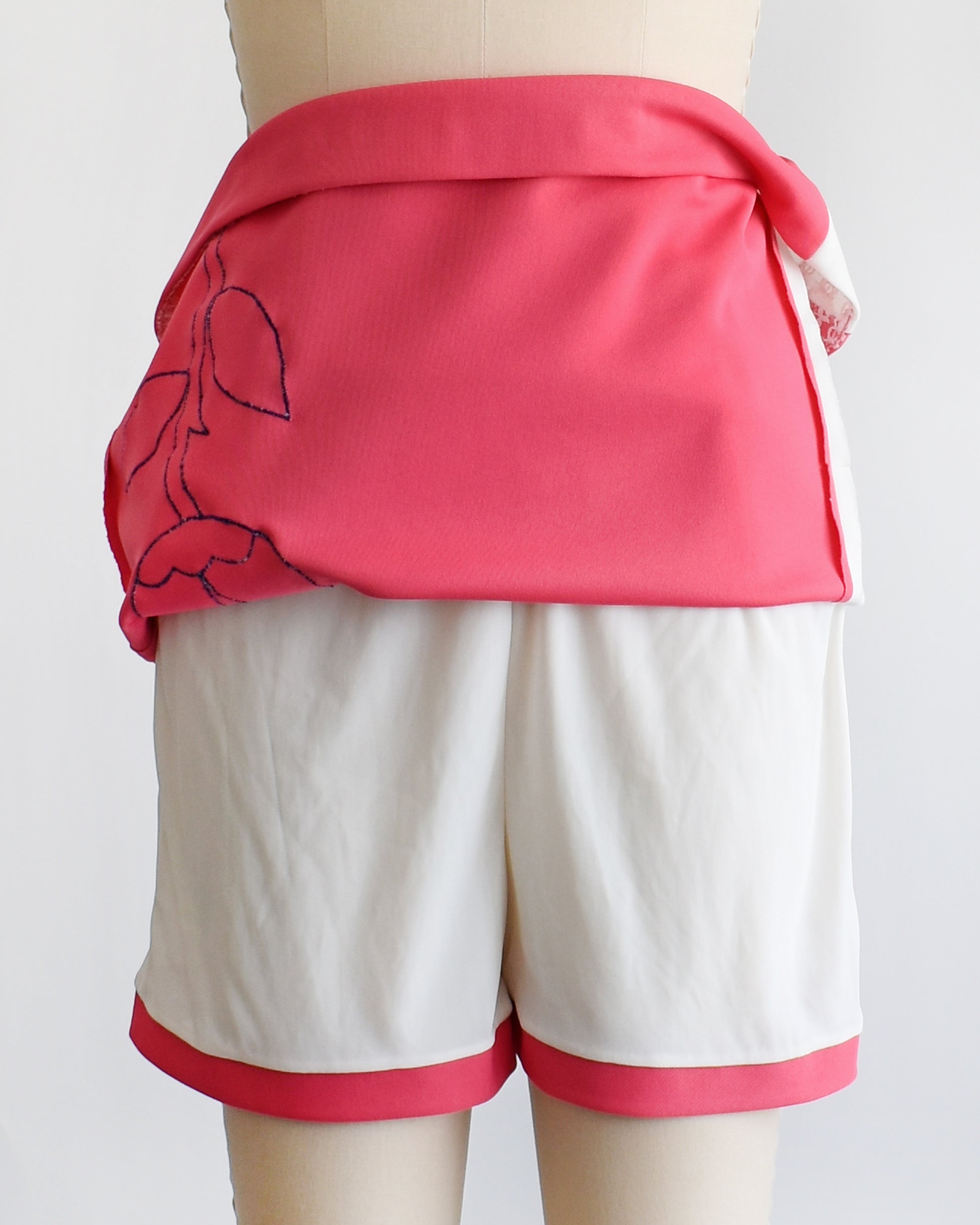 a vintage 1970s pink skirt/skort with a white tulip design with the skirt pulled up showing the shorts underneath on a mannequin against a white background