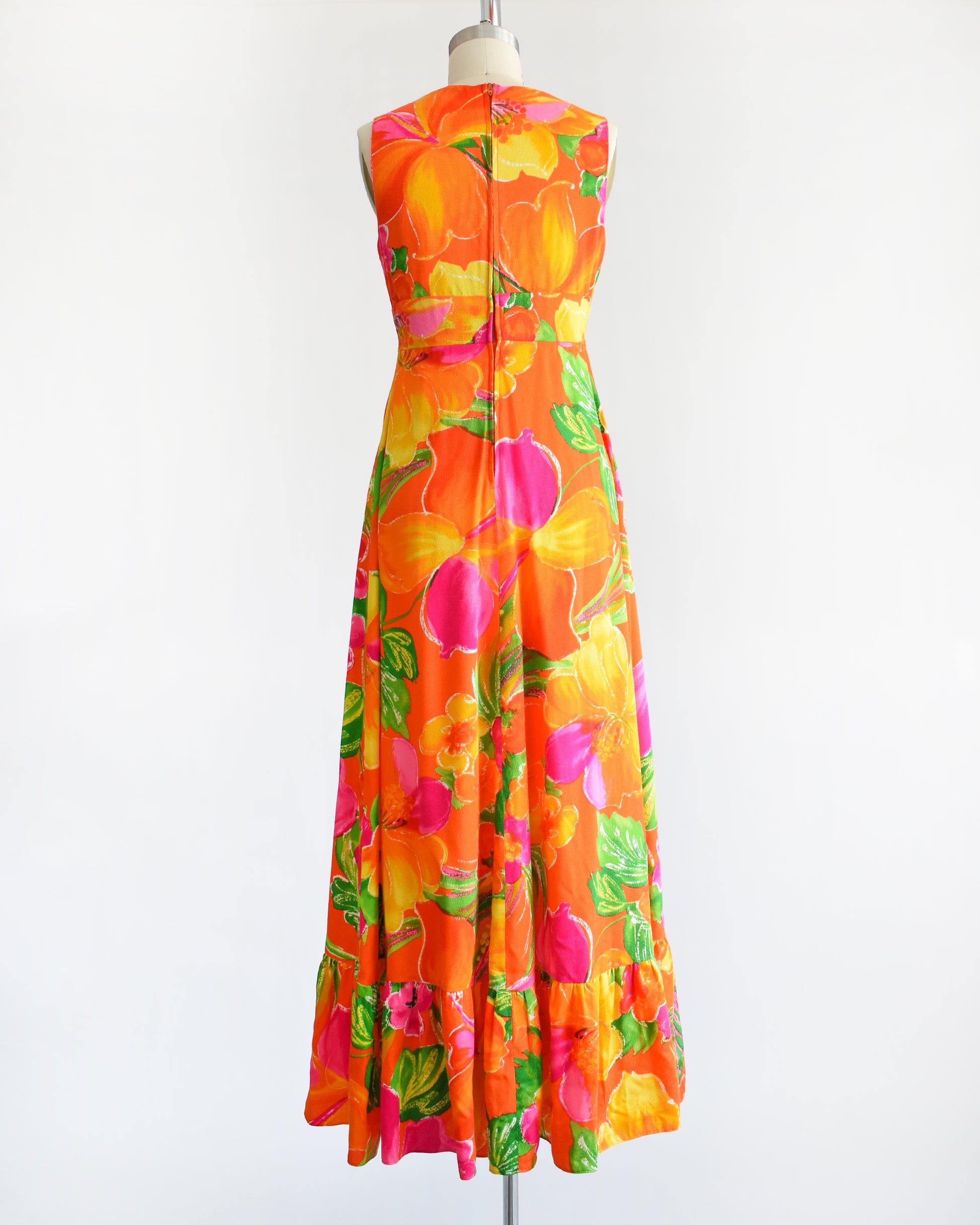 back view of a vintage 1970s Hawaiian maxi dress that has bold floral print in various shades of oranges, pinks, greens, and white.