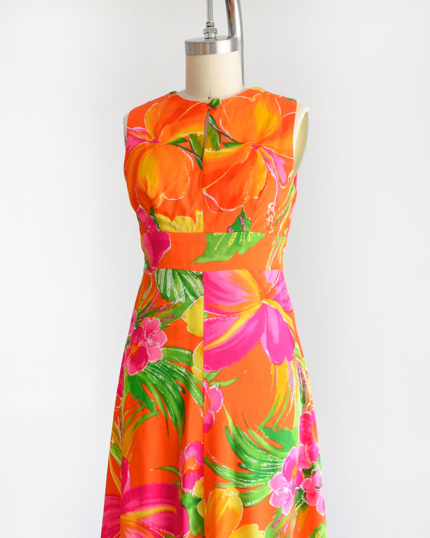 side front view of a vintage 1970s Hawaiian maxi dress that has bold floral print in various shades of oranges, pinks, greens, and white.