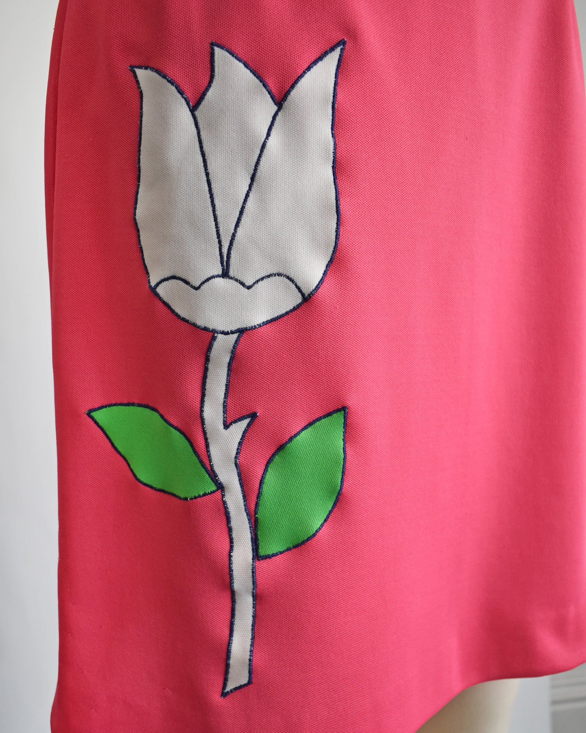 close up of the tulip on a vintage 1970s pink skirt/skort with a white tulip design on a mannequin against a white background