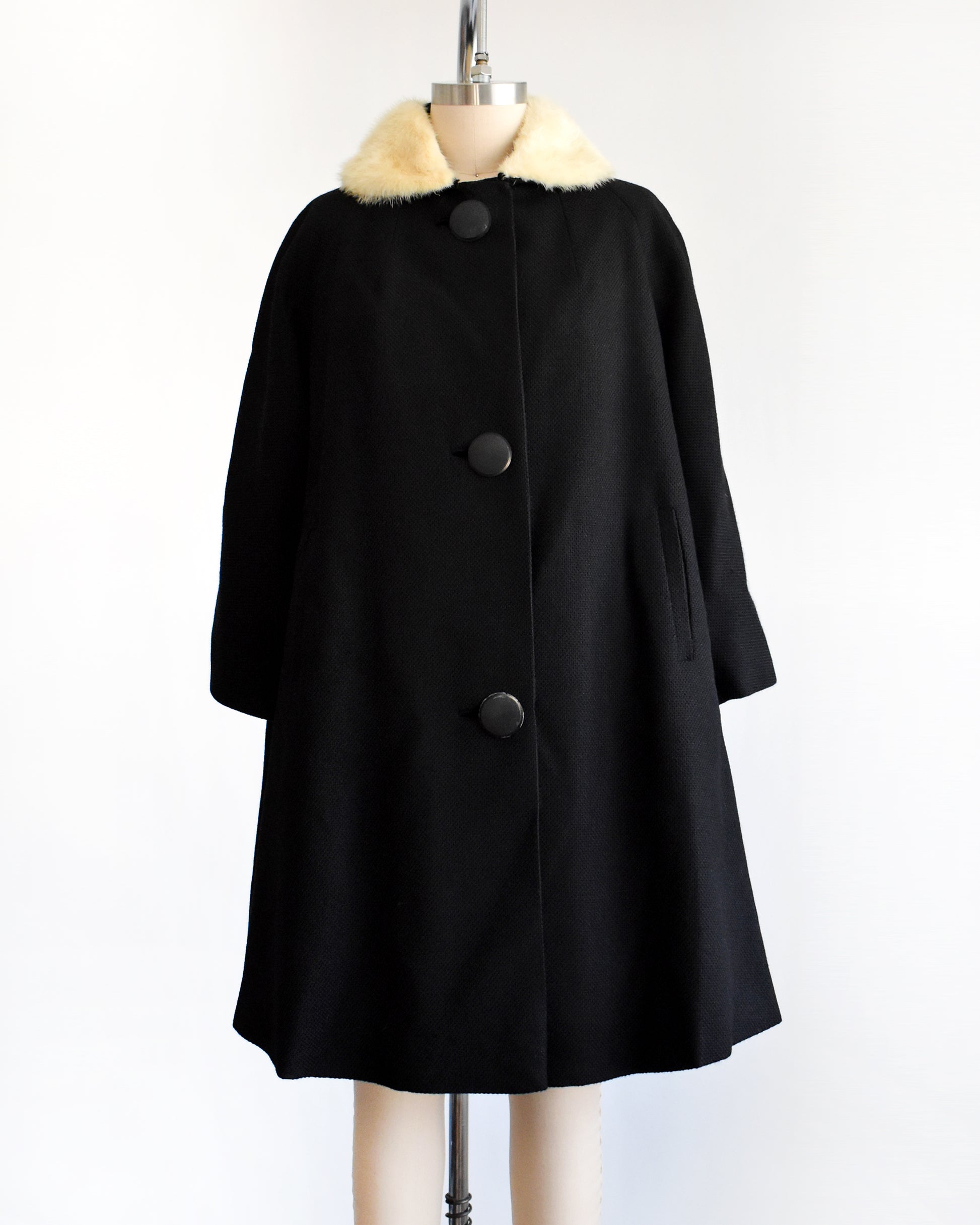 a vintage 1950s black wool coat with fur collar on a mannequin against a white background