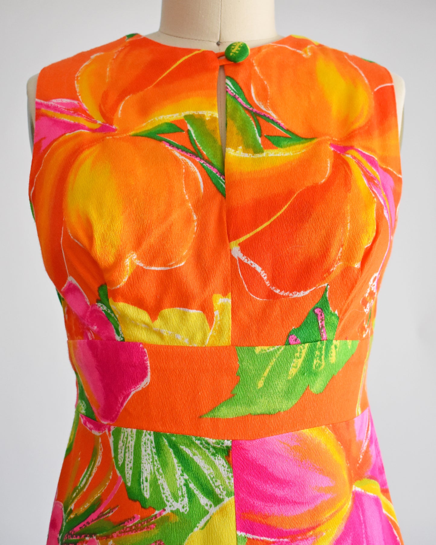 close up of the bodice of a vintage 1970s Hawaiian maxi dress that has bold floral print in various shades of oranges, pinks, greens, and white. The bodice has a button at the center of the neckline and a keyhole opening underneath