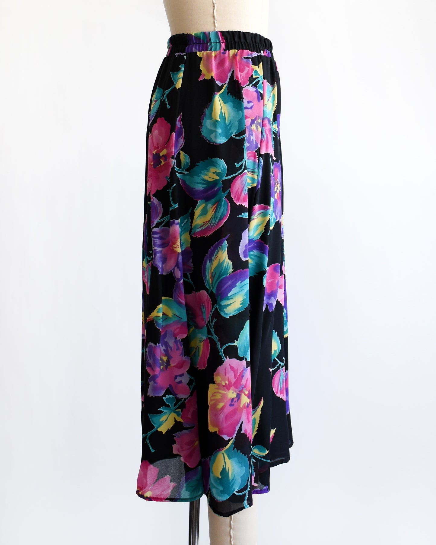 side view of a vintage 1990s black skirt with colorful floral pattern on a mannequin against a white background