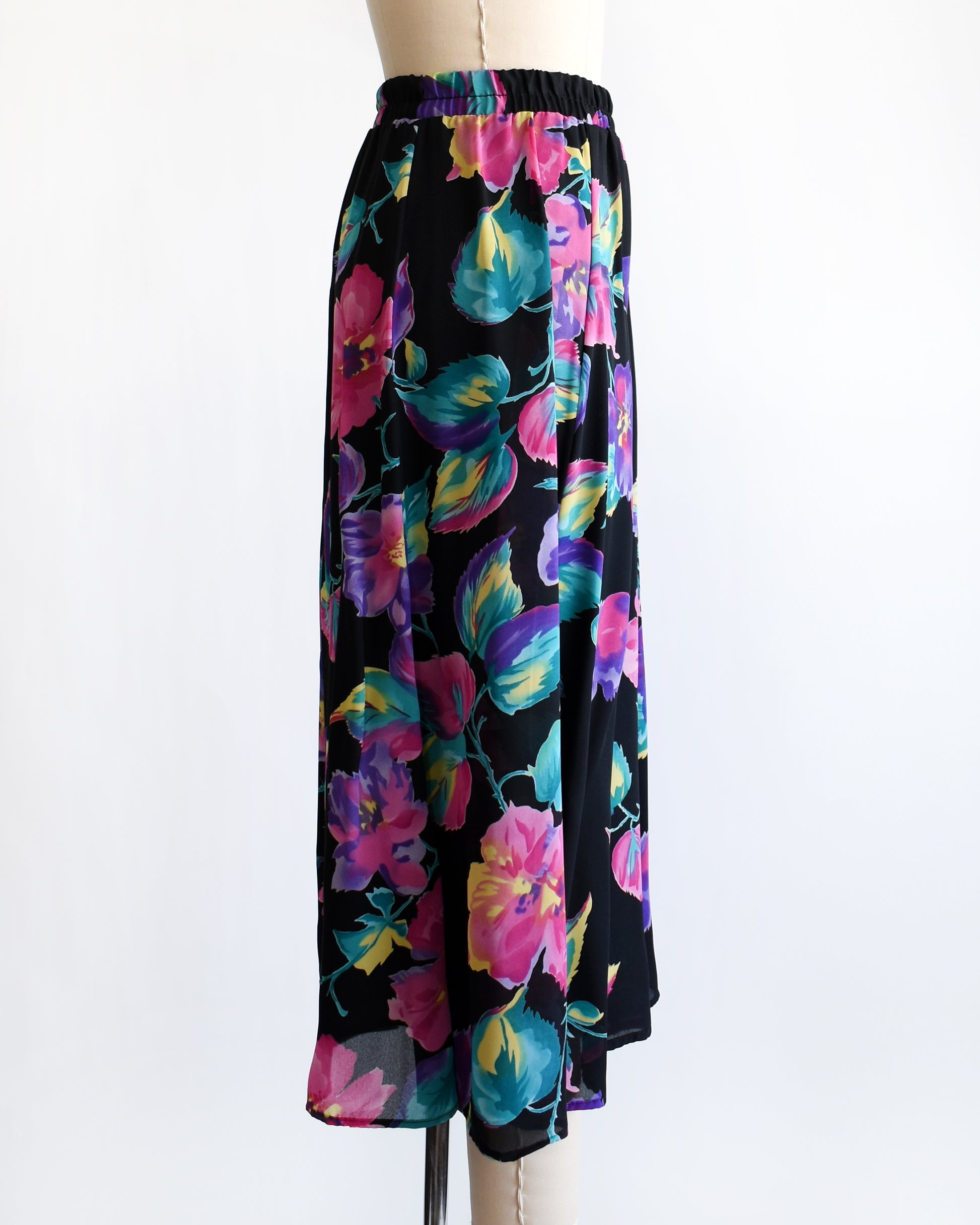 side view of a vintage 1990s black skirt with colorful floral pattern on a mannequin against a white background