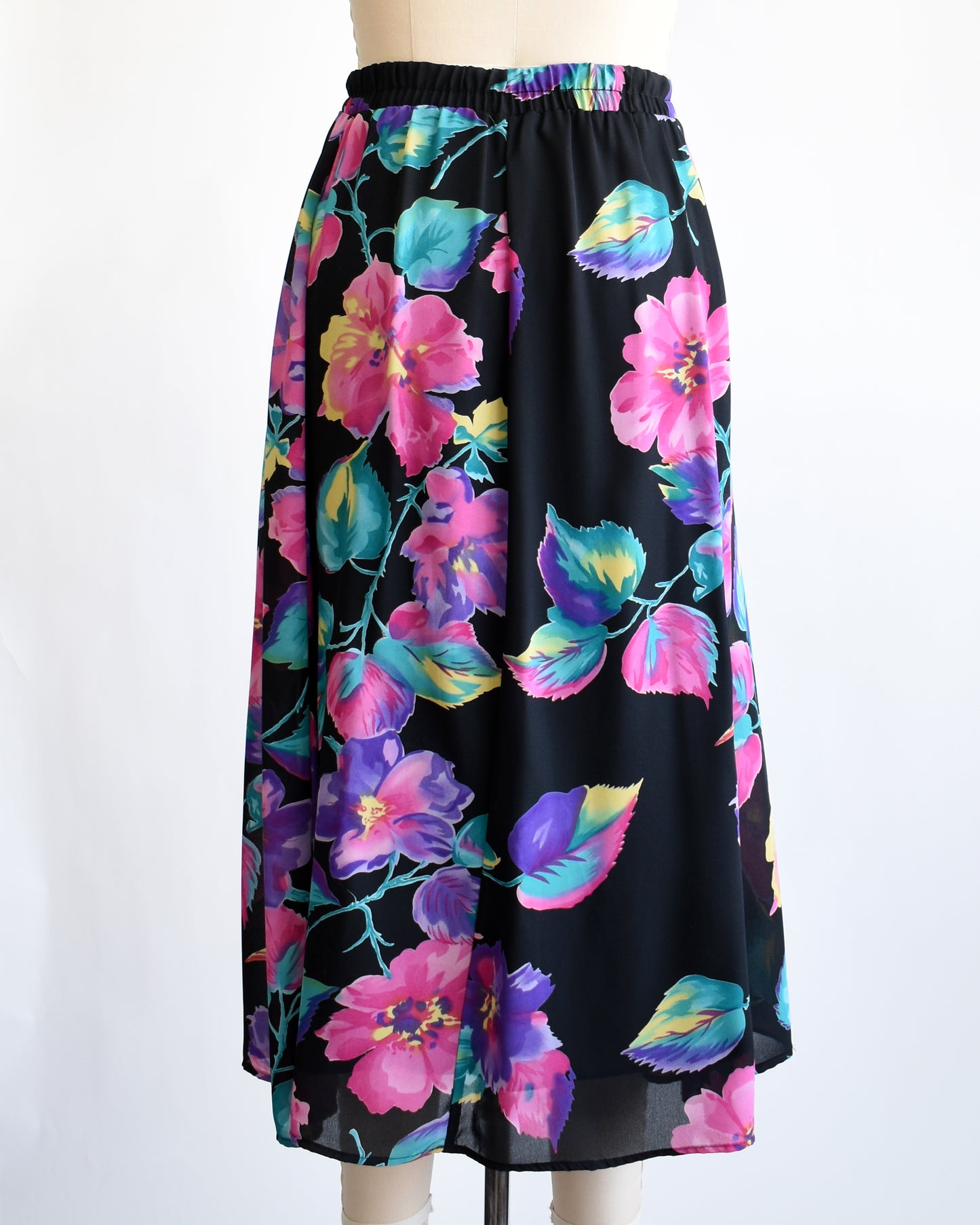 back view of a vintage 1990s black skirt with colorful floral pattern on a mannequin against a white background