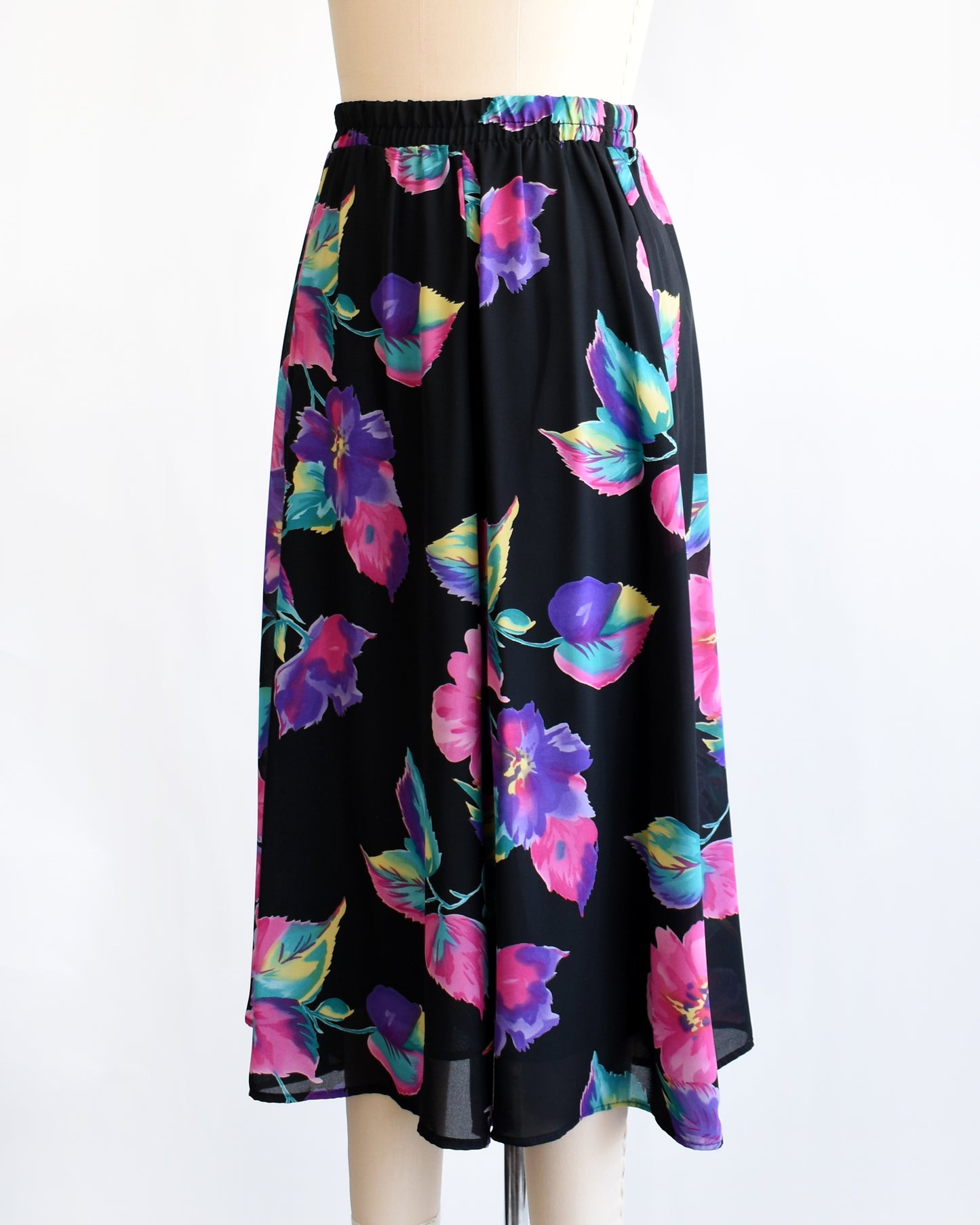 side front view of a vintage 1990s black skirt with colorful floral pattern on a mannequin against a white background
