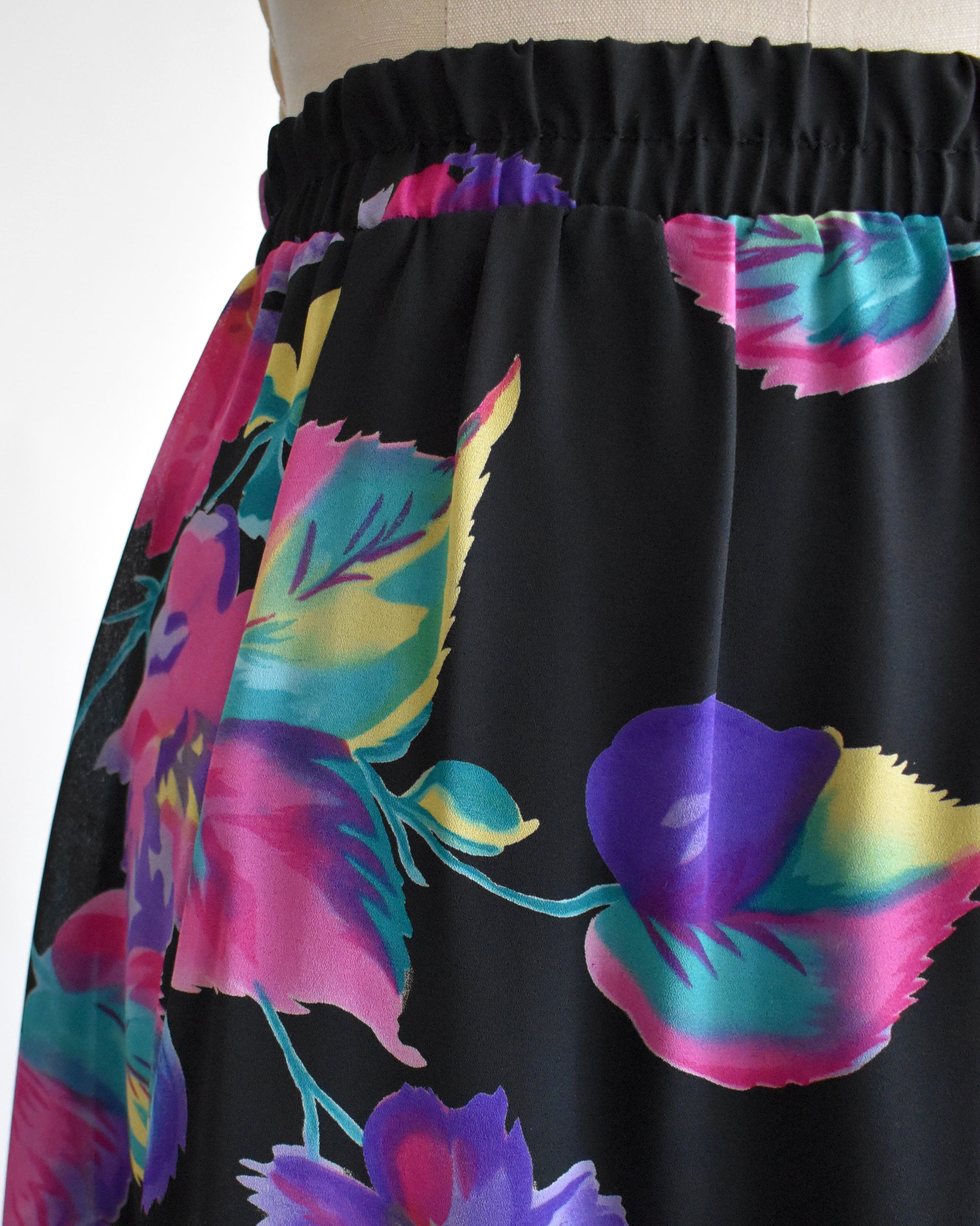 close up of a vintage 1990s black skirt with colorful floral pattern on a mannequin against a white background 