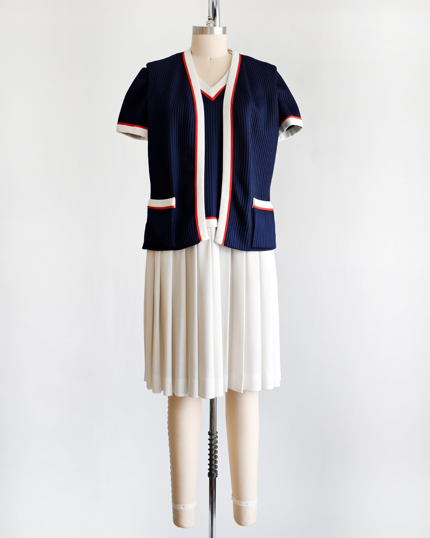 a vintage 1970s navy and white dress set that has red trim and a white skirt on a mannequin on a white background