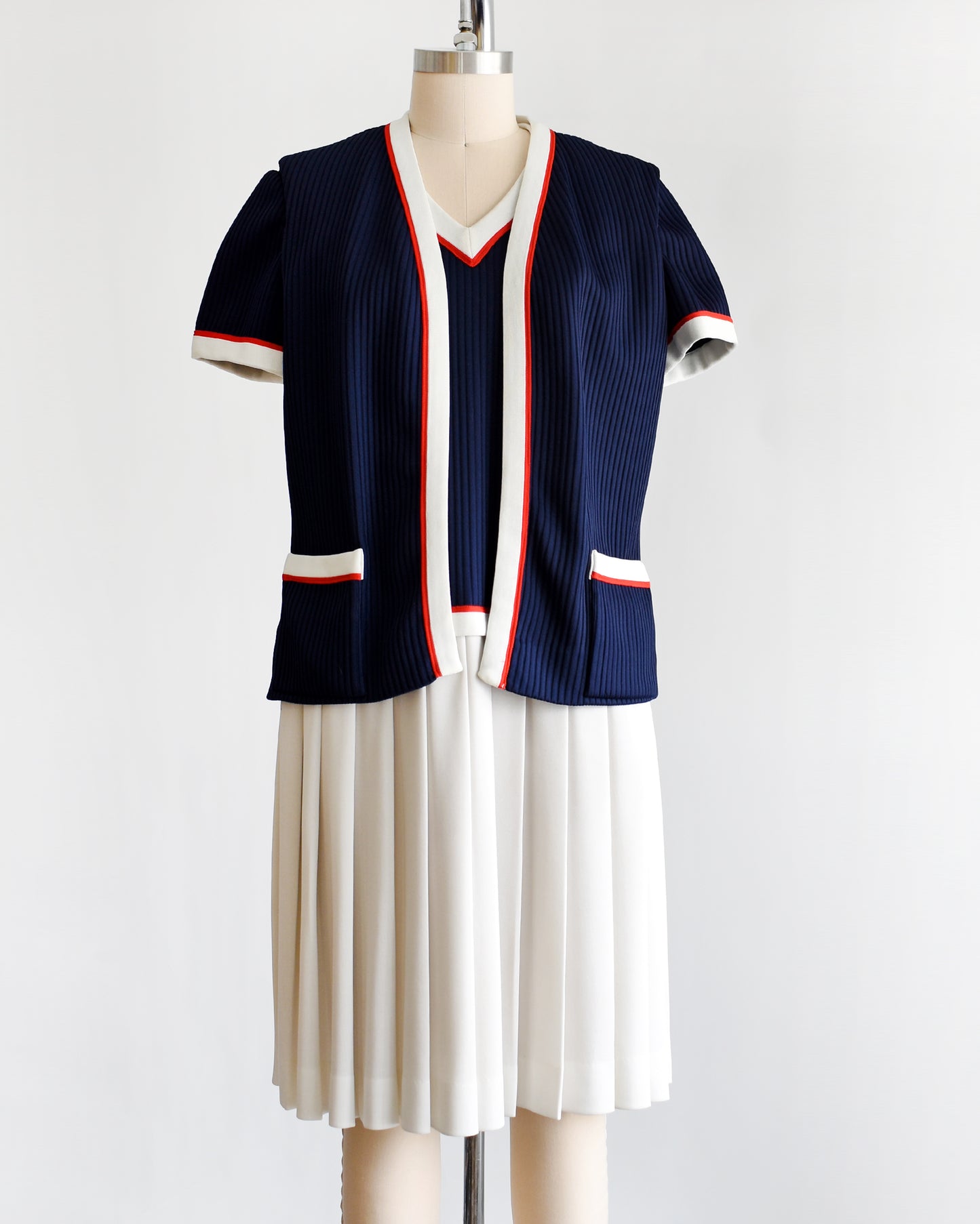a vintage 1970s navy and white dress set that has red trim and a white skirt on a mannequin on a white background