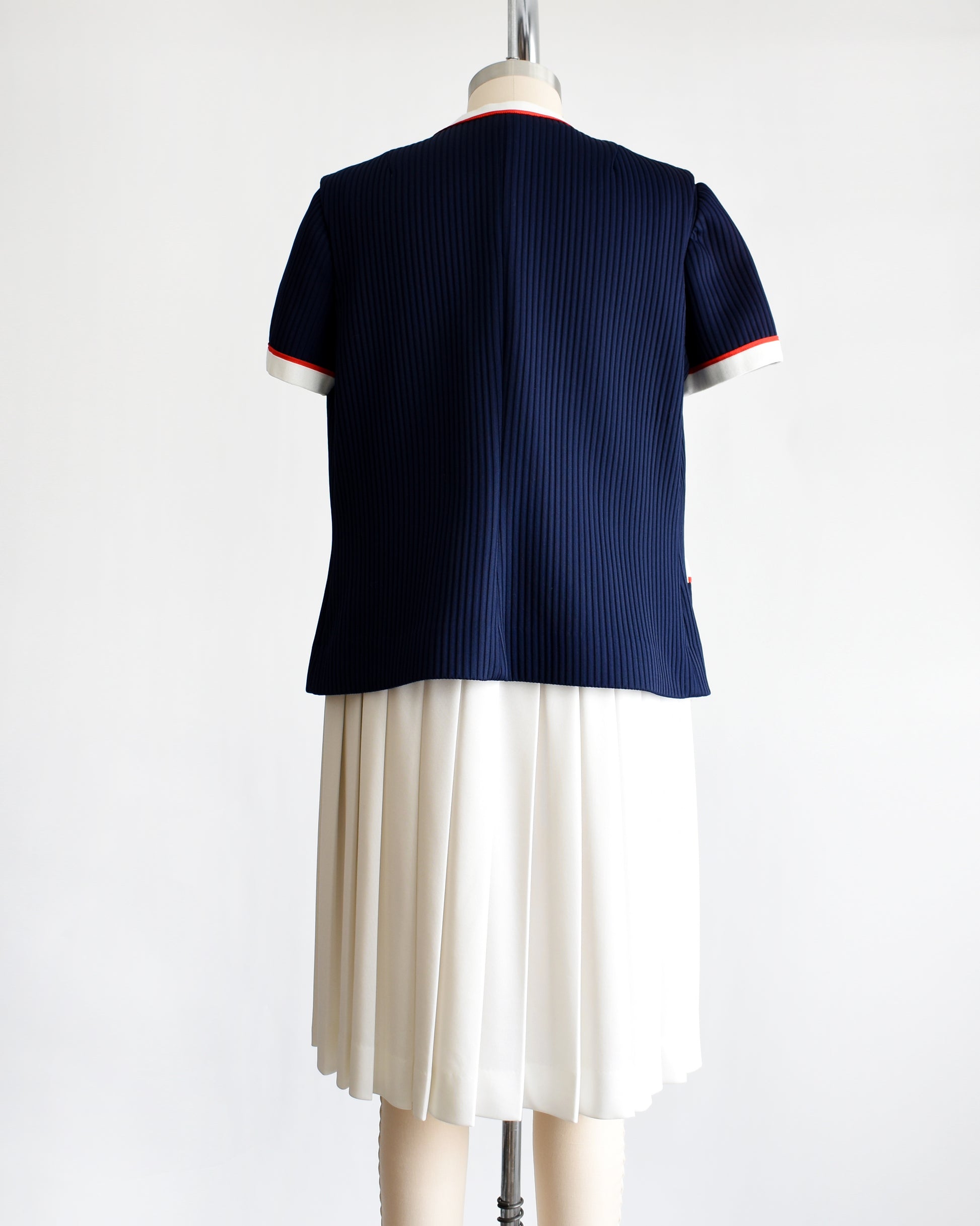 back view of a vintage 1970s navy and white dress set that has red trim and a white skirt on a mannequin on a white background