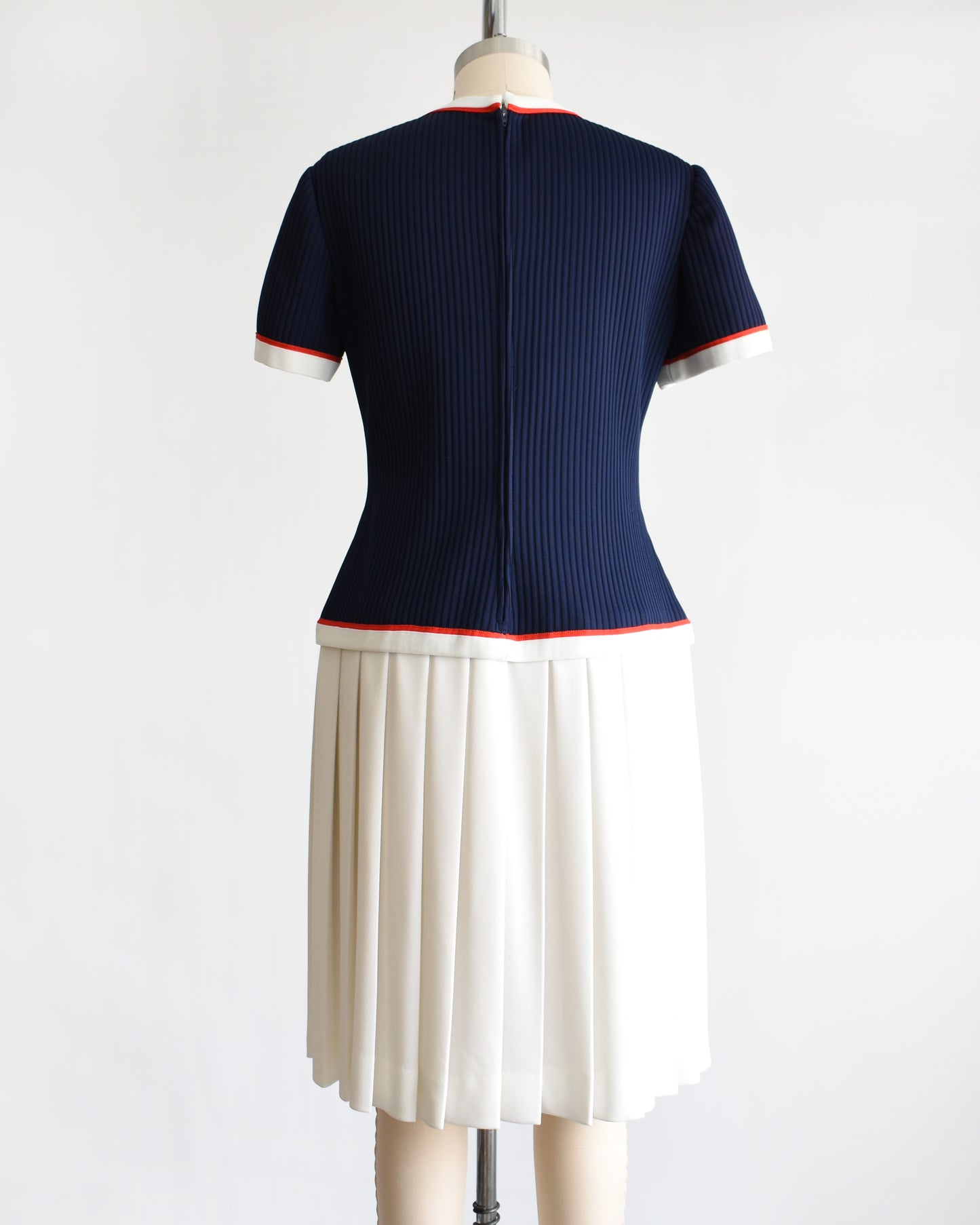 back view of a vintage 1970s navy and white dress set that has red trim and a white skirt on a mannequin on a white background. the vest is off in this photo