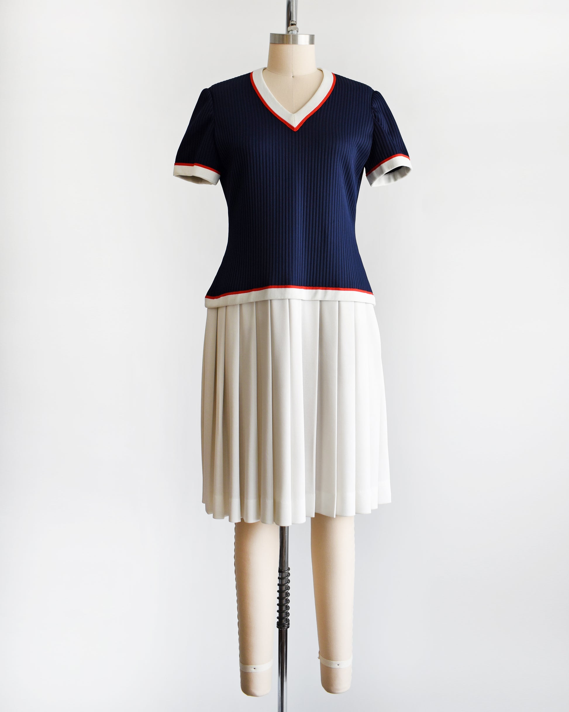 a vintage 1970s navy and white dress that has red trim and a white skirt on a mannequin on a white background