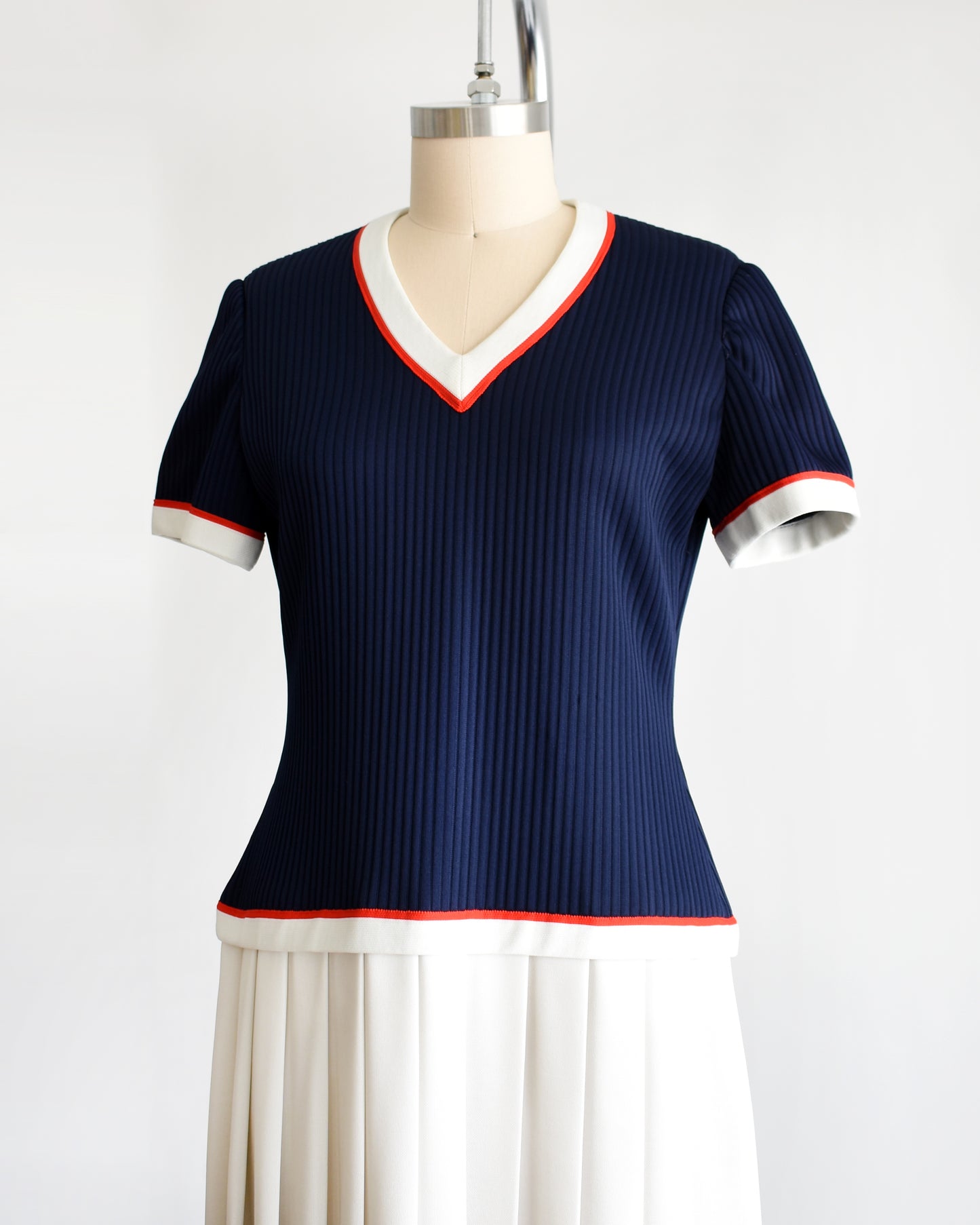 side view of a vintage 1970s navy and white dress set that has red trim and a white skirt on a mannequin on a white background. the vest is off in this photo