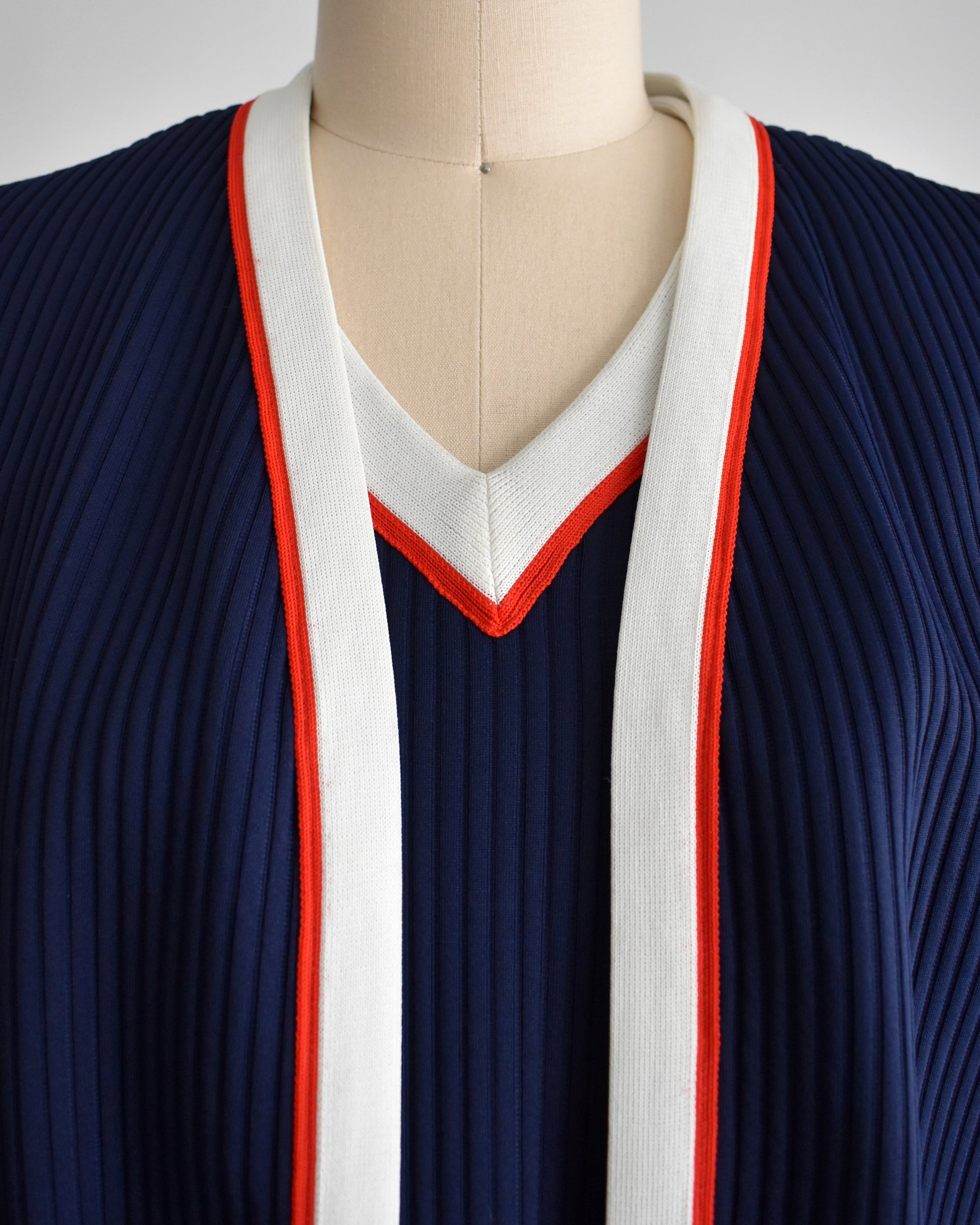 a close up of a vintage 1970s navy and white dress set that has red trim and a white skirt on a mannequin on a white background