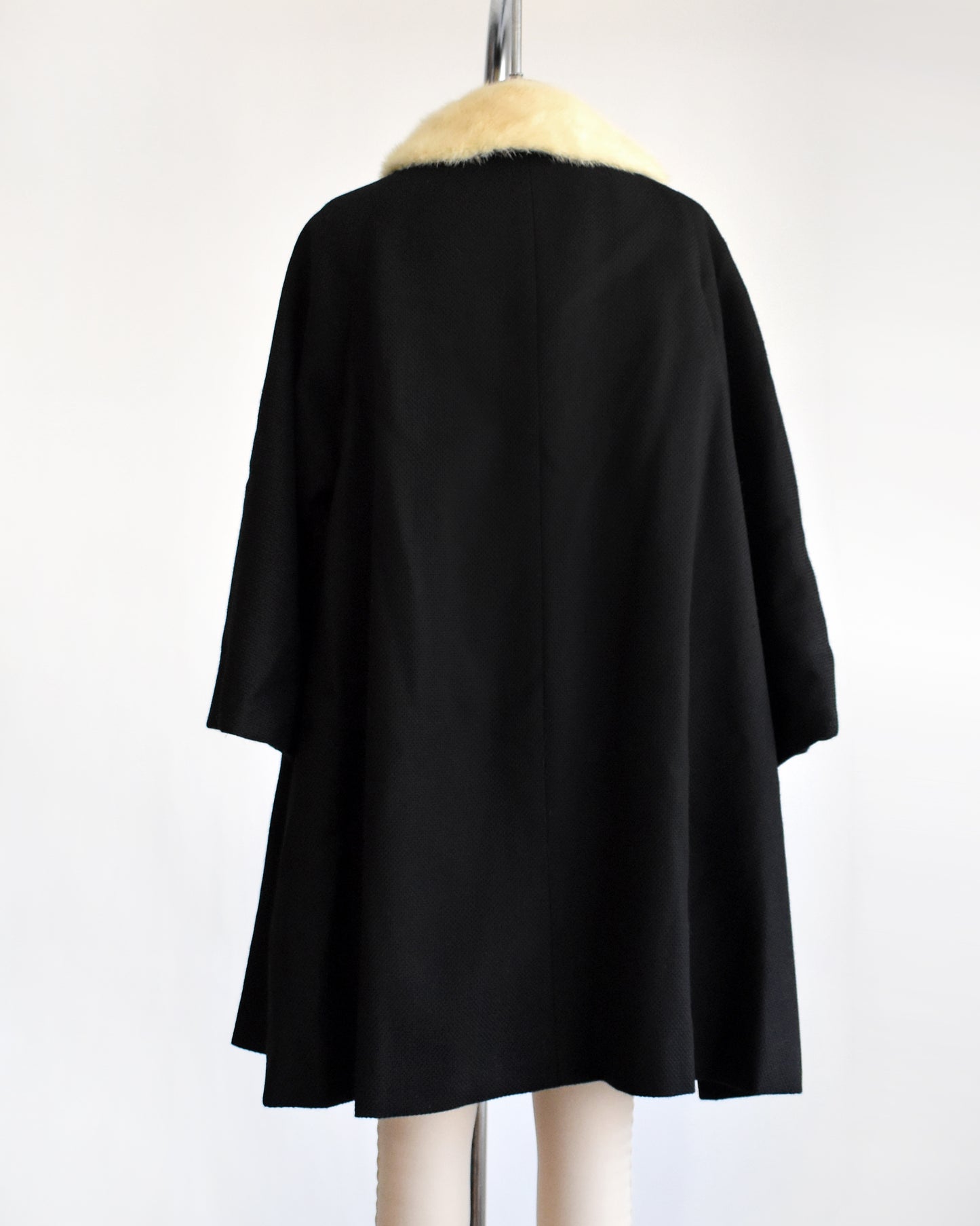 back view of a vintage 1950s black wool coat with fur collar on a mannequin against a white background