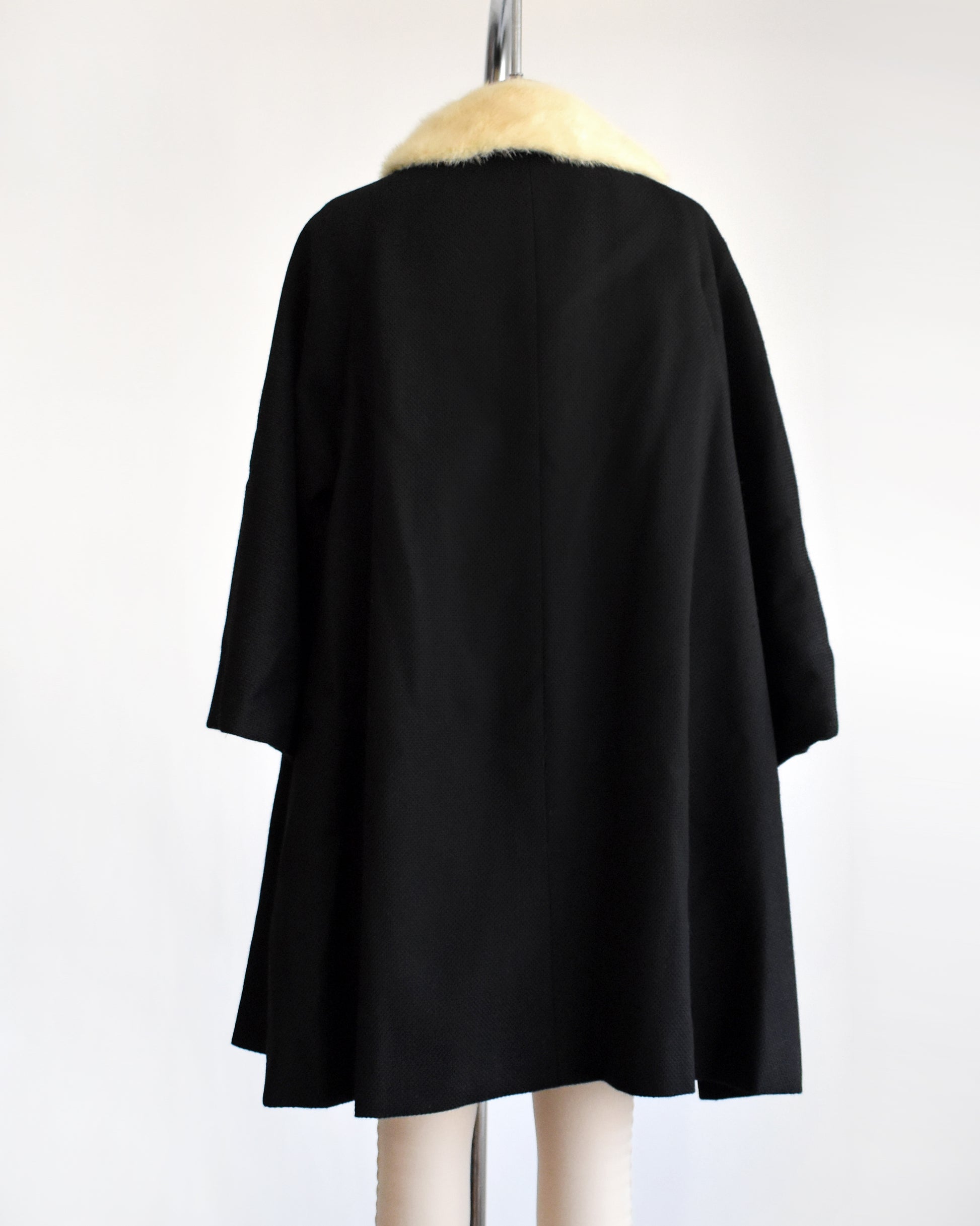 back view of a vintage 1950s black wool coat with fur collar on a mannequin against a white background