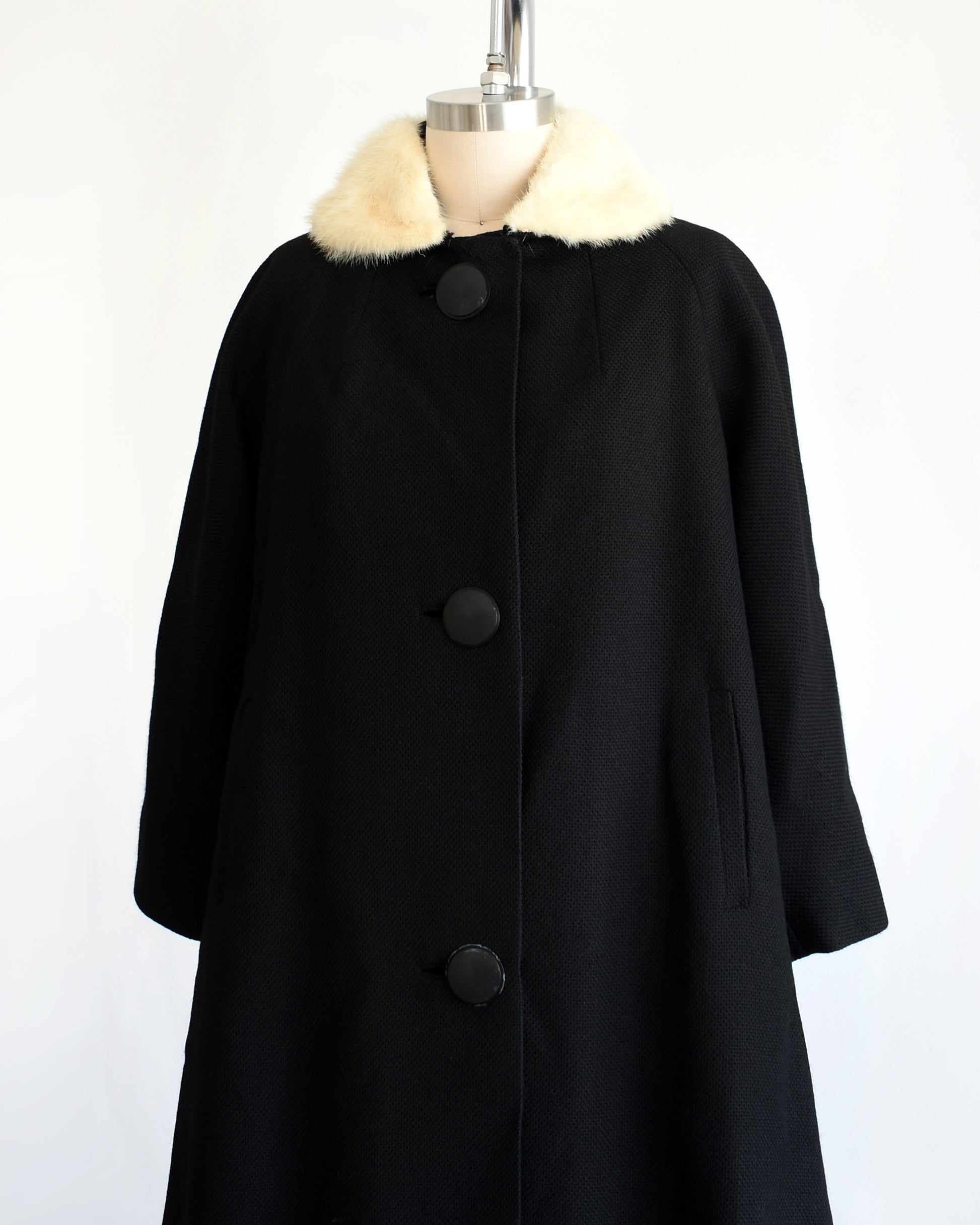 side front view of a vintage 1950s black wool coat with fur collar on a mannequin against a white background