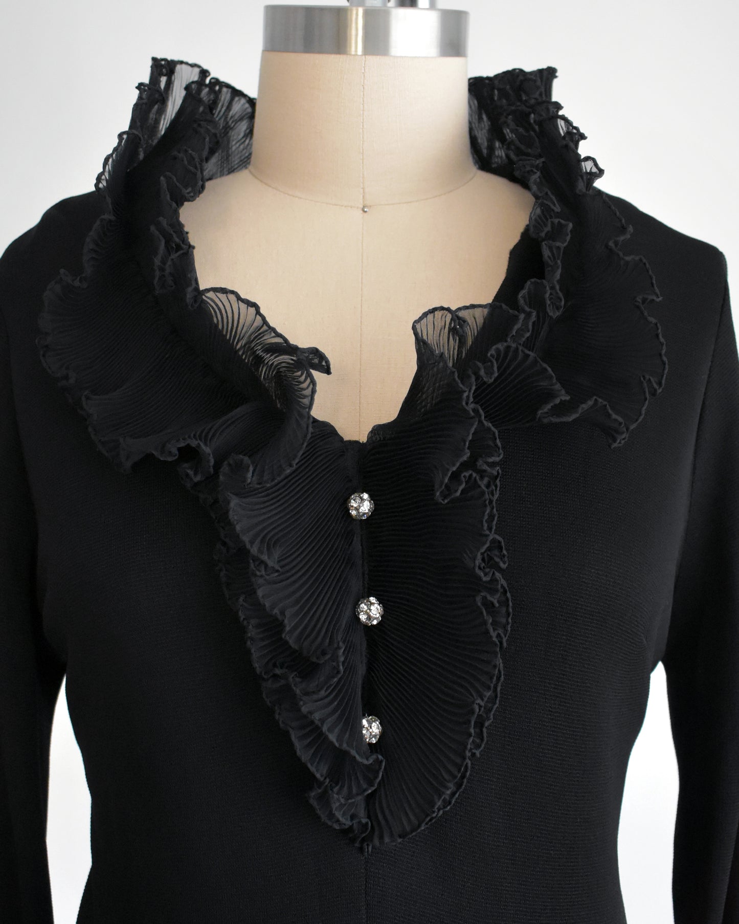 close up of the ruffled neckline on a vintage 1970s black ruffled pant set with decorative rhinestone buttons