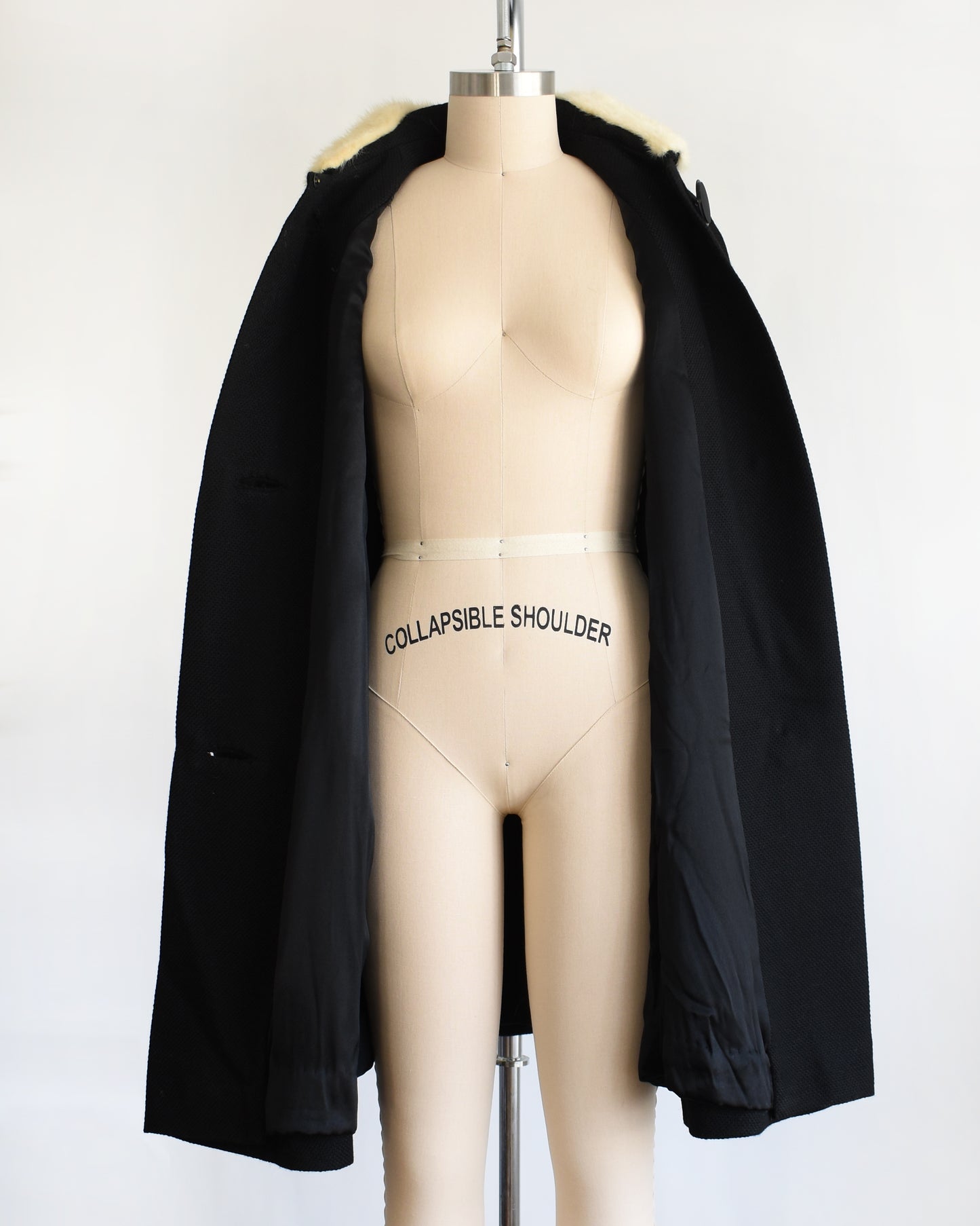 a vintage 1950s black wool coat with fur collar on a mannequin against a white background. The coat is opened in this photo.