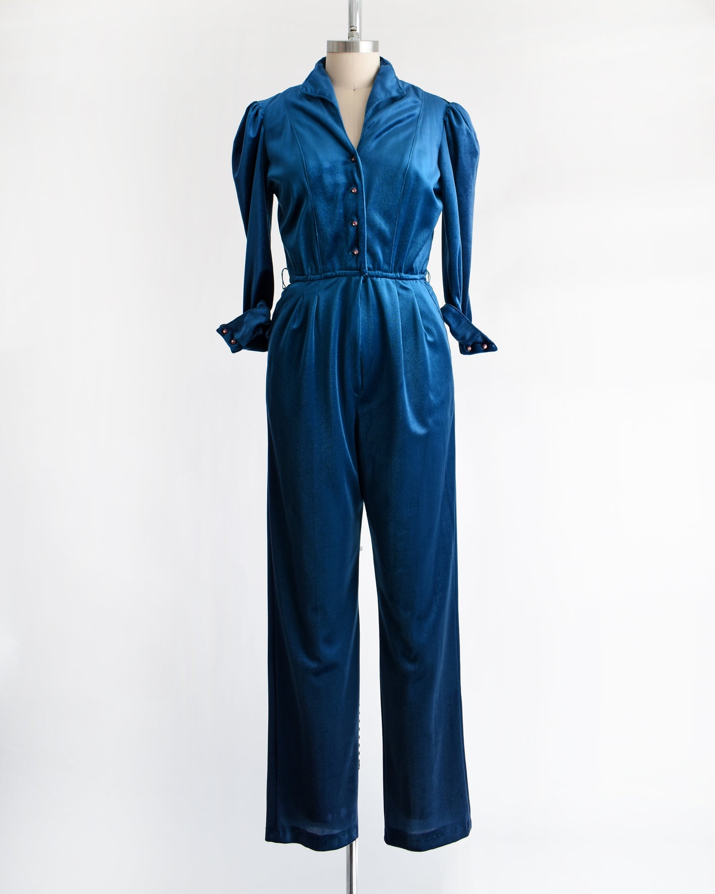 a vintage 1970s blue velour jumpsuit on a mannequin against a white background