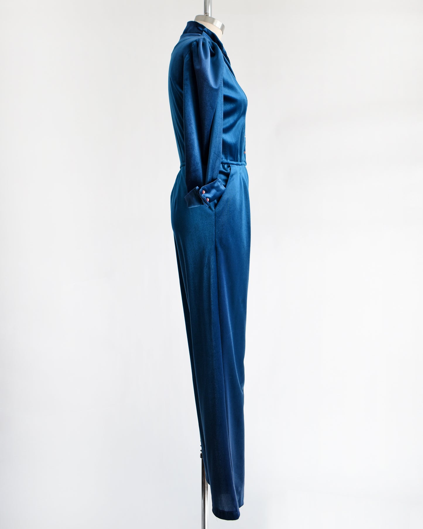 side view of a vintage 1970s blue velour jumpsuit on a mannequin against a white background