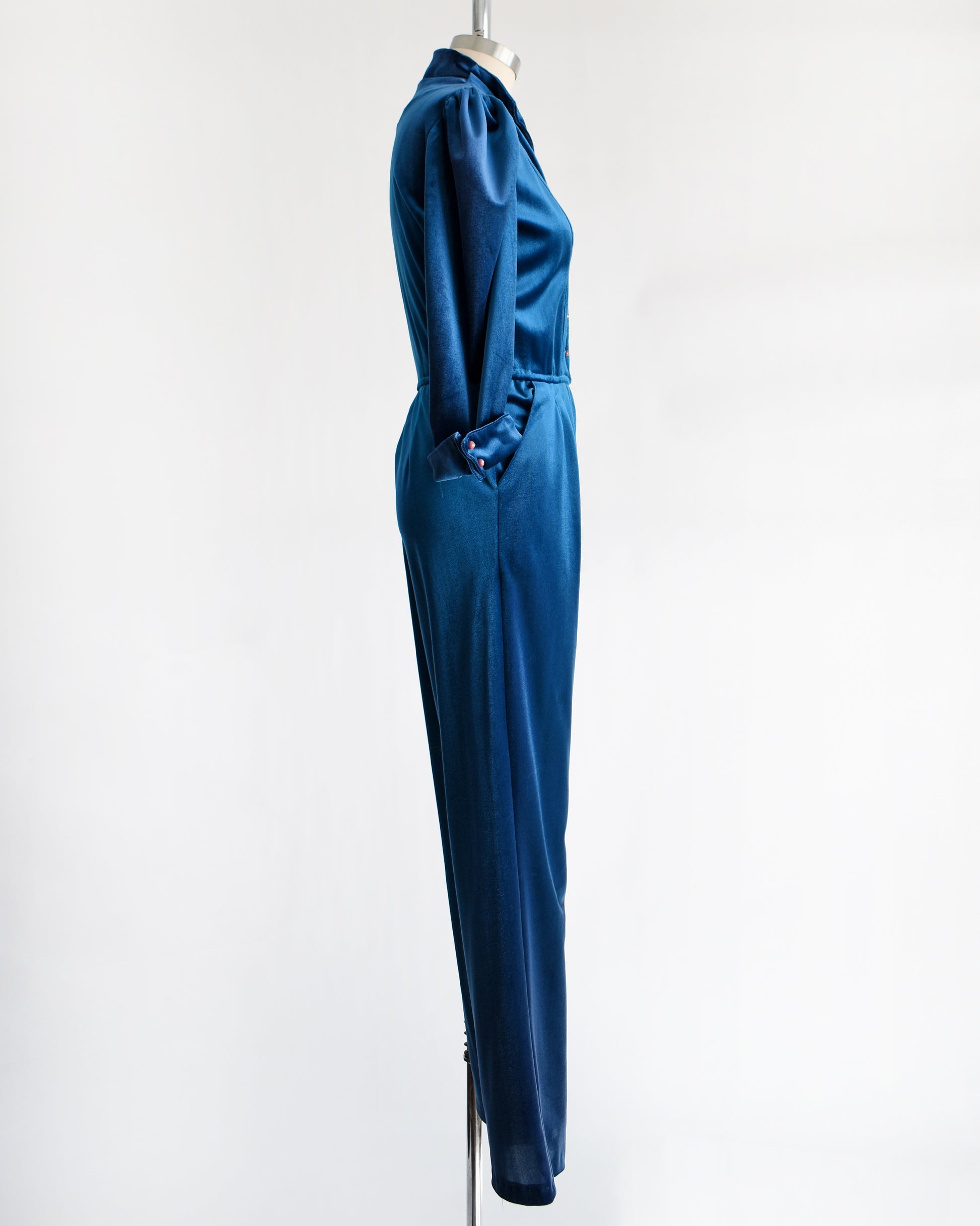 side view of a vintage 1970s blue velour jumpsuit on a mannequin against a white background