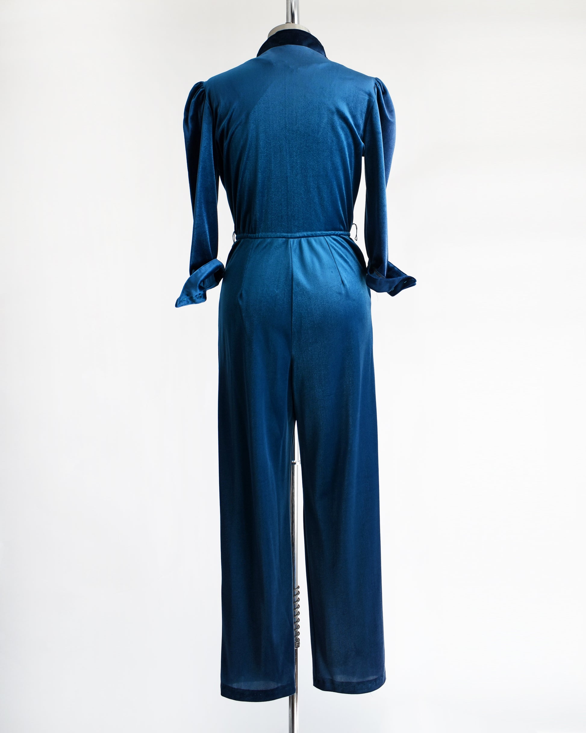 back view of a vintage 1970s blue velour jumpsuit on a mannequin against a white background